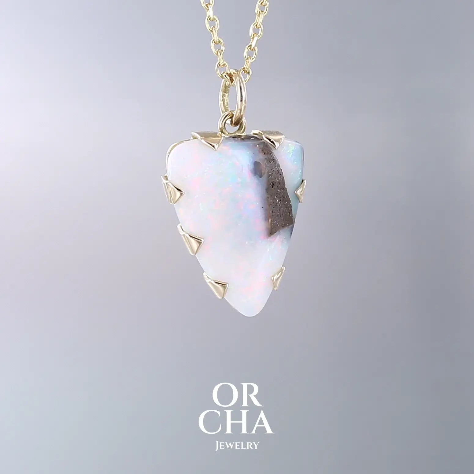 Pendentif pour femme en or jaune massif 18k serti d'une opale boulder aux feux multicolores. Majoritairement blanche une inclusion de matrice brune ressort en surface de la pierre, lui conférant un charme fou. Pierre naturelle taillée en cabochon de forme libre serti de griffe. Bijoux unique, éthique et durable présenté dans un coffret de notre marque, prêt à offrir. Livraison offerte, certificat d'authenticité, service client