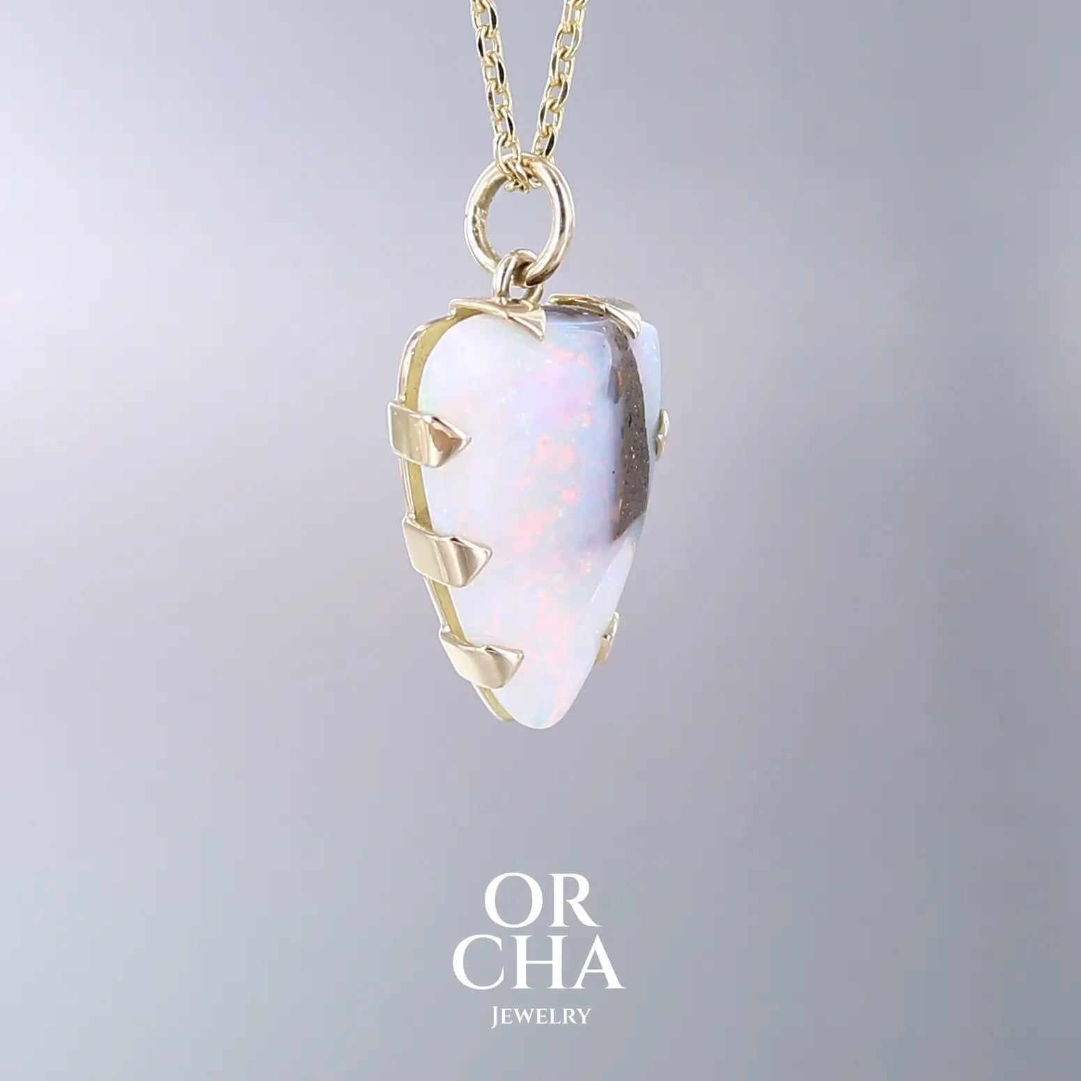 Pendentif pour femme en or jaune massif 18k serti d'une opale boulder aux feux multicolores. Majoritairement blanche une inclusion de matrice brune ressort en surface de la pierre, lui conférant un charme fou. Pierre naturelle taillée en cabochon de forme libre serti de griffe. Bijoux unique, éthique et durable présenté dans un coffret de notre marque, prêt à offrir. Livraison offerte, certificat d'authenticité, service client