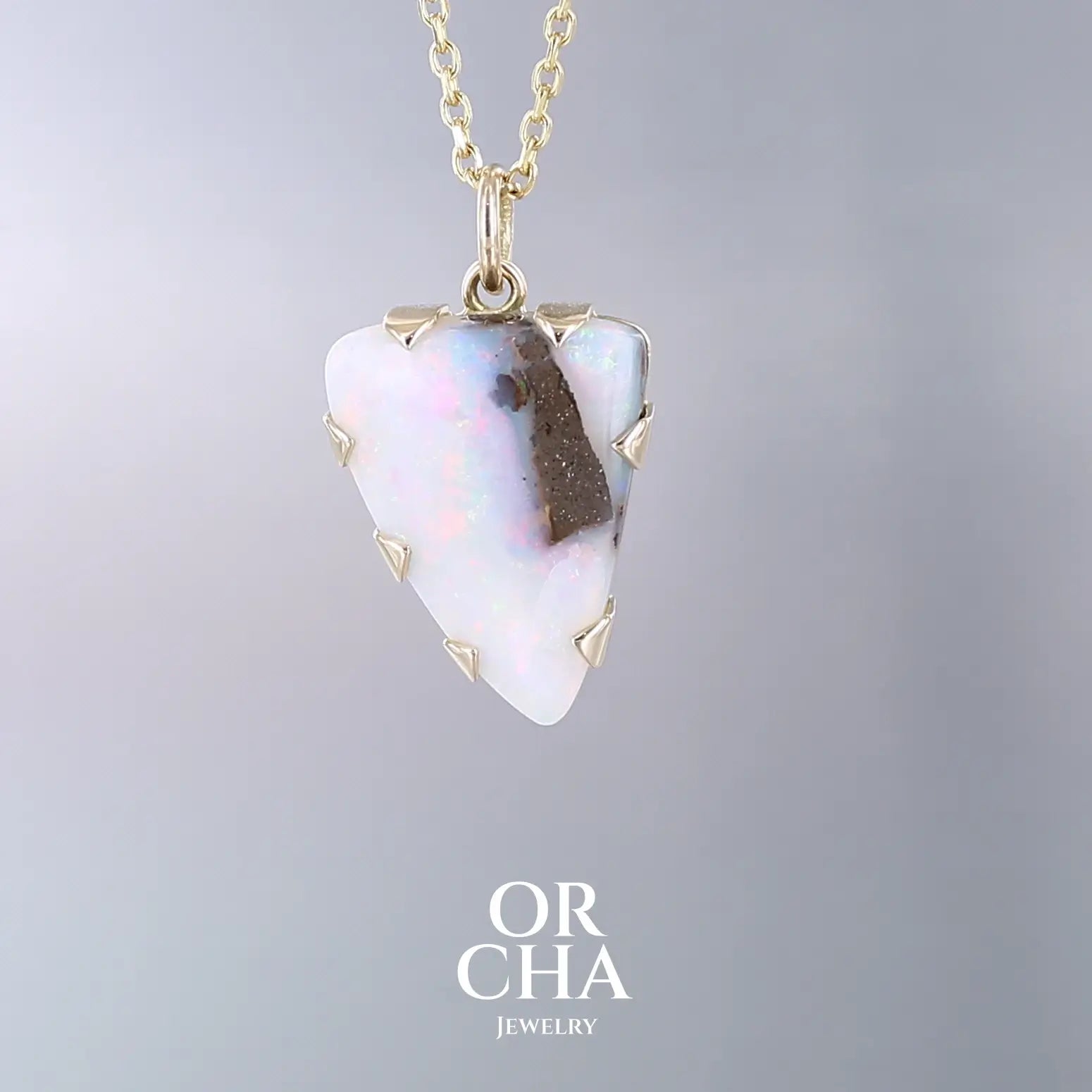 Pendentif pour femme en or jaune massif 18k serti d'une opale boulder aux feux multicolores. Majoritairement blanche une inclusion de matrice brune ressort en surface de la pierre, lui conférant un charme fou. Pierre naturelle taillée en cabochon de forme libre serti de griffe. Bijoux unique, éthique et durable présenté dans un coffret de notre marque, prêt à offrir. Livraison offerte, certificat d'authenticité, service client