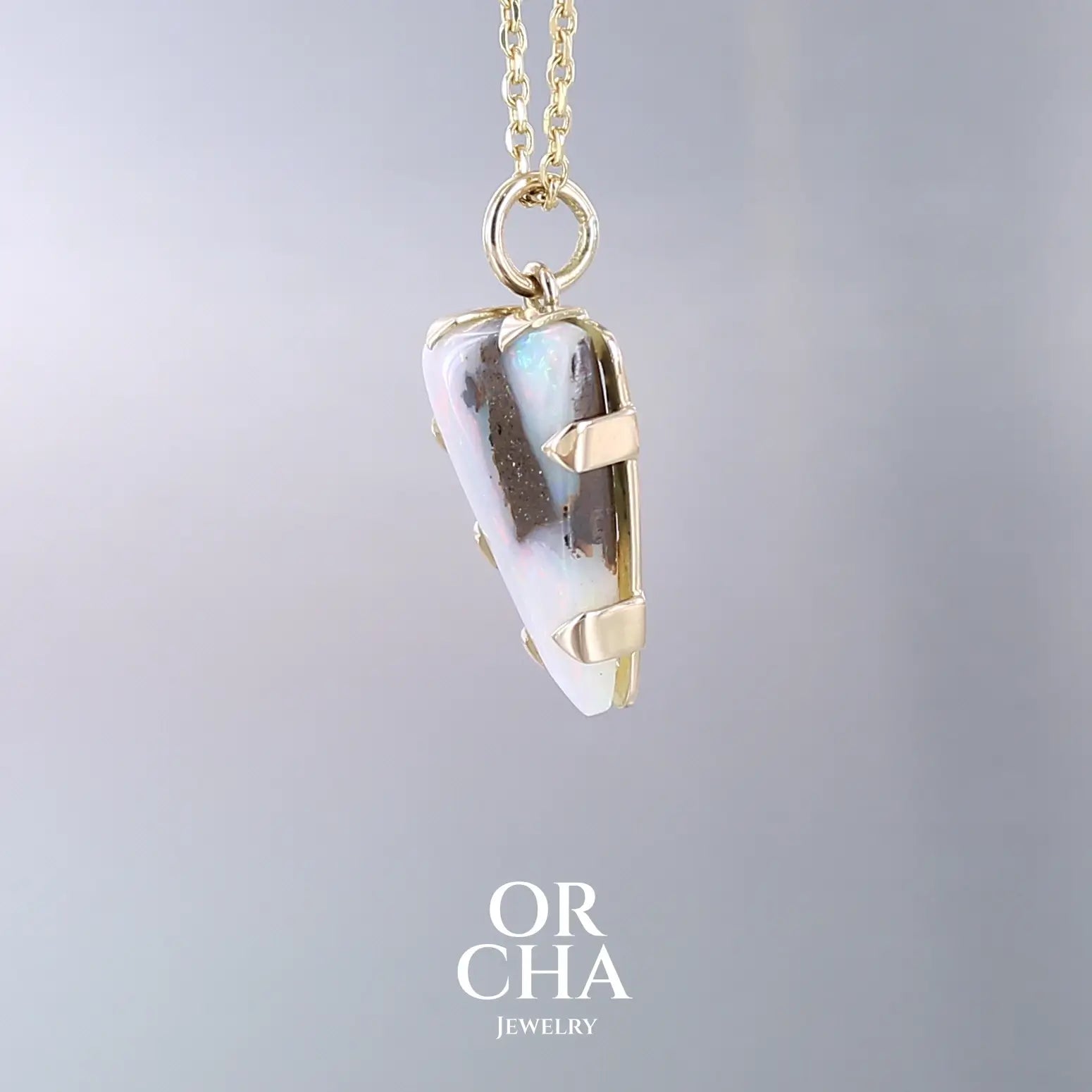 Pendentif pour femme en or jaune massif 18k serti d'une opale boulder aux feux multicolores. Majoritairement blanche une inclusion de matrice brune ressort en surface de la pierre, lui conférant un charme fou. Pierre naturelle taillée en cabochon de forme libre serti de griffe. Bijoux unique, éthique et durable présenté dans un coffret de notre marque, prêt à offrir. Livraison offerte, certificat d'authenticité, service client