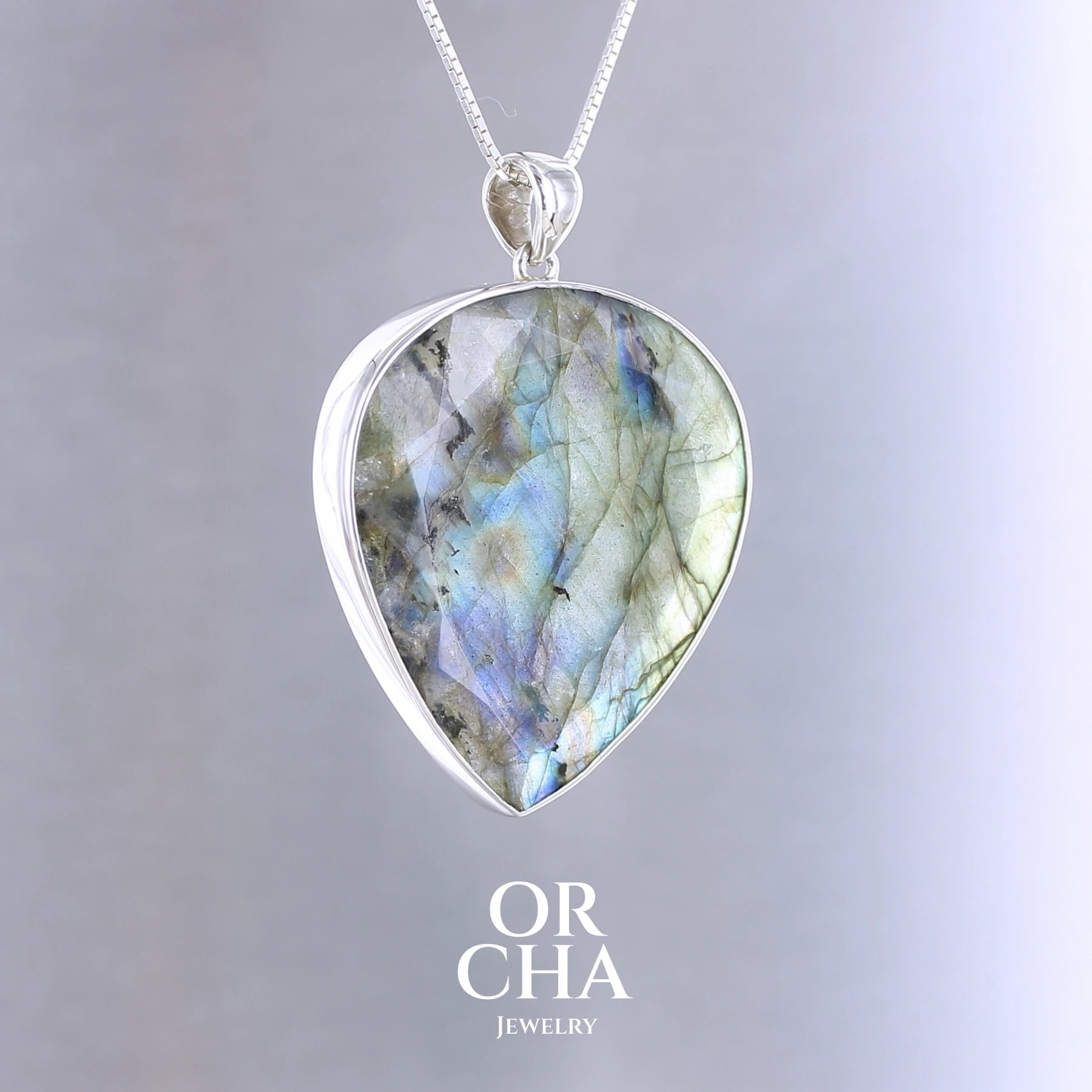 Pendentif pour femme en argent massif sertie d'une labradorite aux reflets bleus et bronze selon la lumière. Pierre facettée naturelle translucide présentant des inclusions fréquents sur ce type de pierre. Bijoux unique, éthique et durable présenté dans un coffret de notre marque, prêt à offrir. Livraison offerte, certificat d'authenticité, service client.