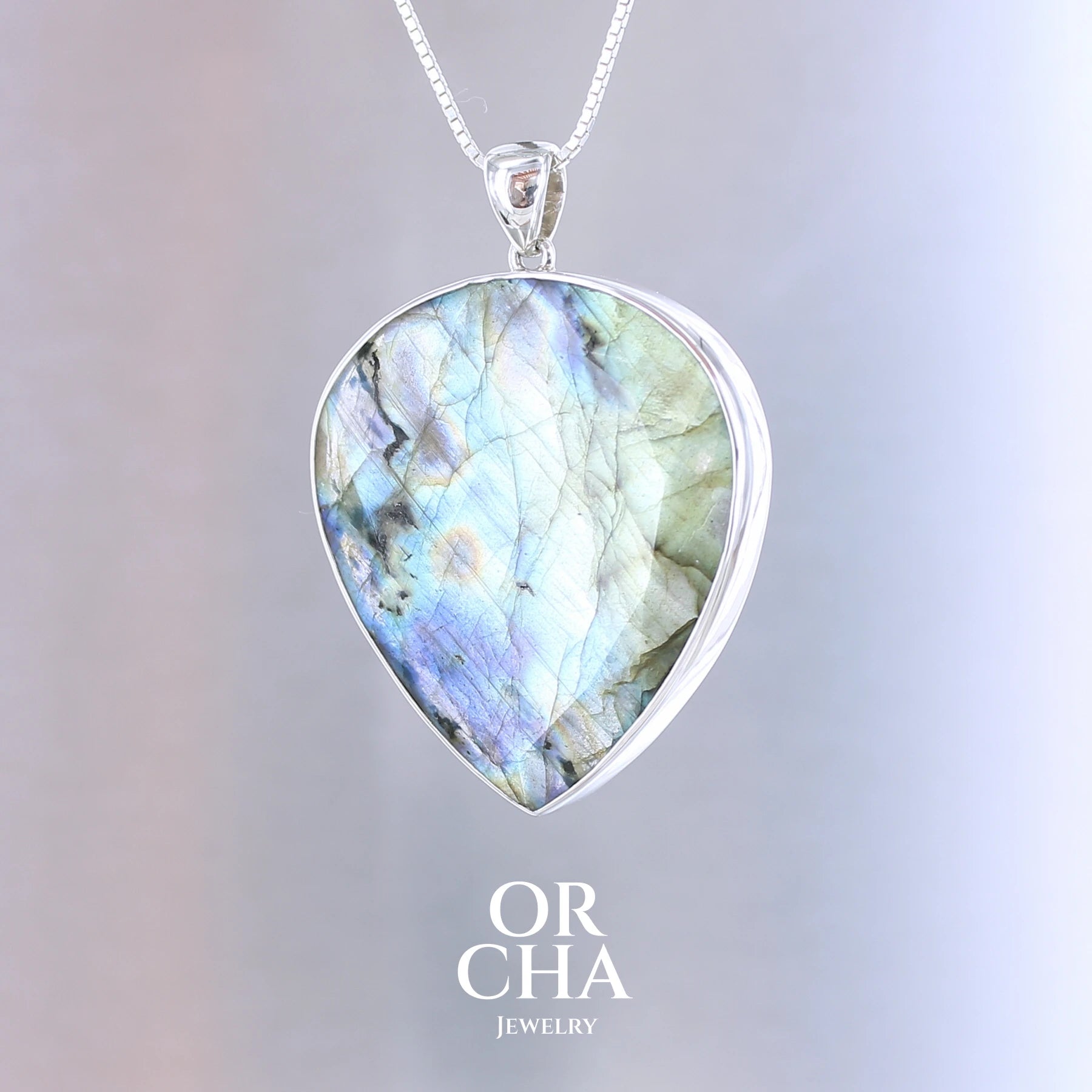 Pendentif pour femme en argent massif sertie d'une labradorite aux reflets bleus et bronze selon la lumière. Pierre facettée naturelle translucide présentant des inclusions fréquents sur ce type de pierre. Bijoux unique, éthique et durable présenté dans un coffret de notre marque, prêt à offrir. Livraison offerte, certificat d'authenticité, service client.