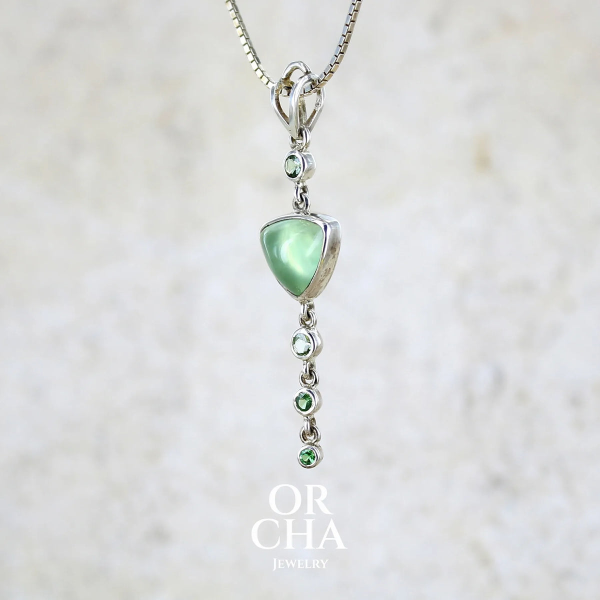 Pendentif pour femme en argent massif sertie d'un cabochon triangulaire de Préhnite ainsi que de petites tourmalines vertes formant une cascade colorée vert pastel lumineux. Pierre transparente à inclusions. Bijou unique réalisé par Orchajewelry
