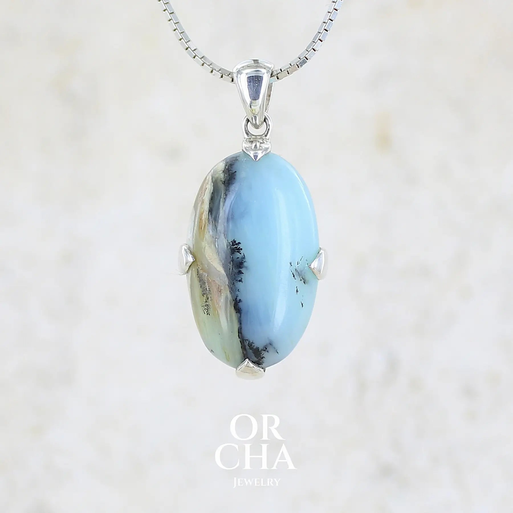 Pendentif pour femme et homme en argent massif, sertie d'un cabochon ovale d'opale bleue du Pérou de couleur bleu laiteux à inclusions de dendrites paysages noires et de roche mère marron. Pierre opaque et translucide. Bijoux unique, éthique et durable présenté dans un coffret de notre marque, prêt à offrir. Livraison offerte, certificat d'authenticité, service client.
