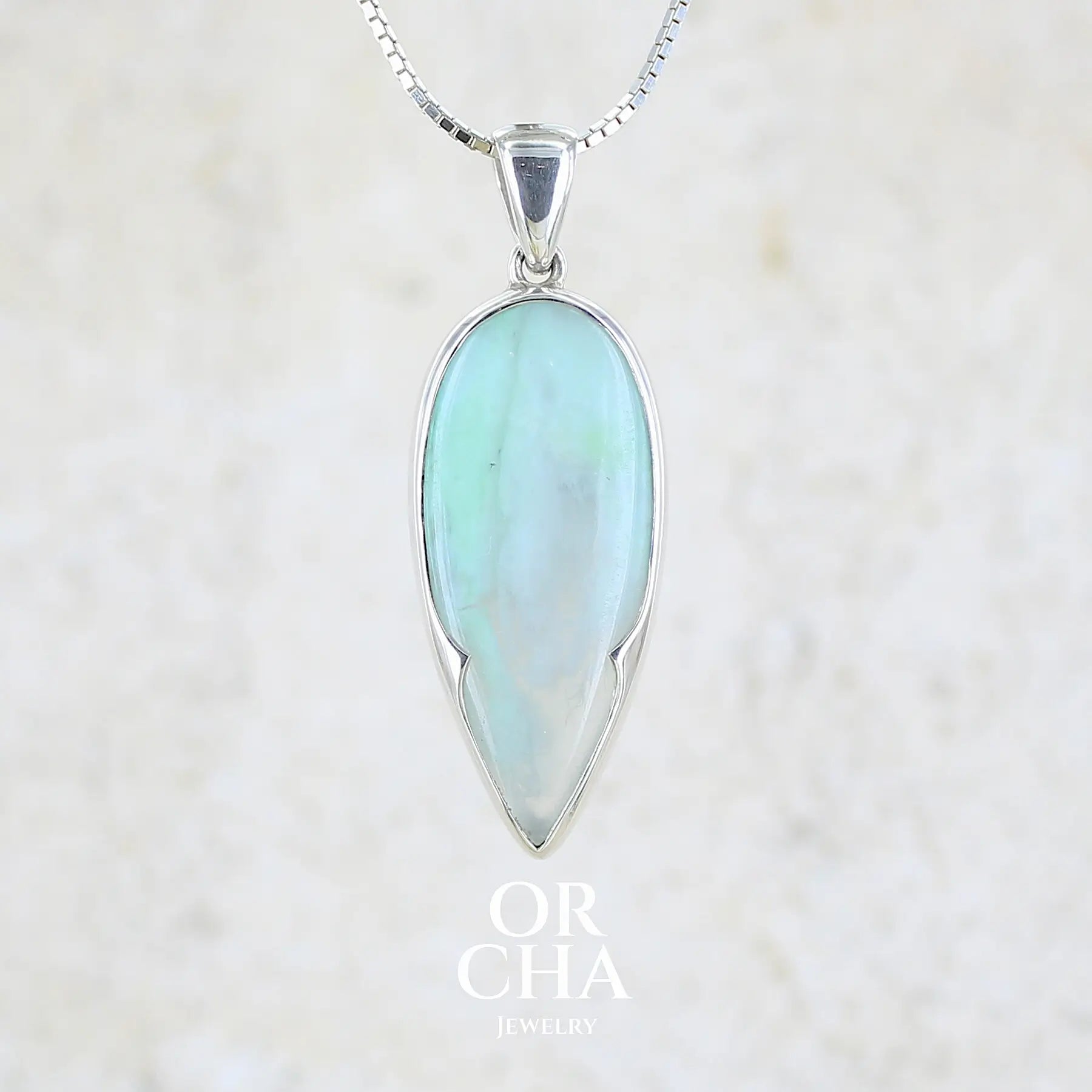 Pendentif pour femme et homme en argent massif, sertie d'un cabochon d'opale bleue du Pérou de couleur verte bleutée. Pierre en forme de goutte inversée. Pierre opaque et translucide. Bijoux unique, éthique et durable présenté dans un coffret de notre marque, prêt à offrir. Livraison offerte, certificat d'authenticité, service client.
