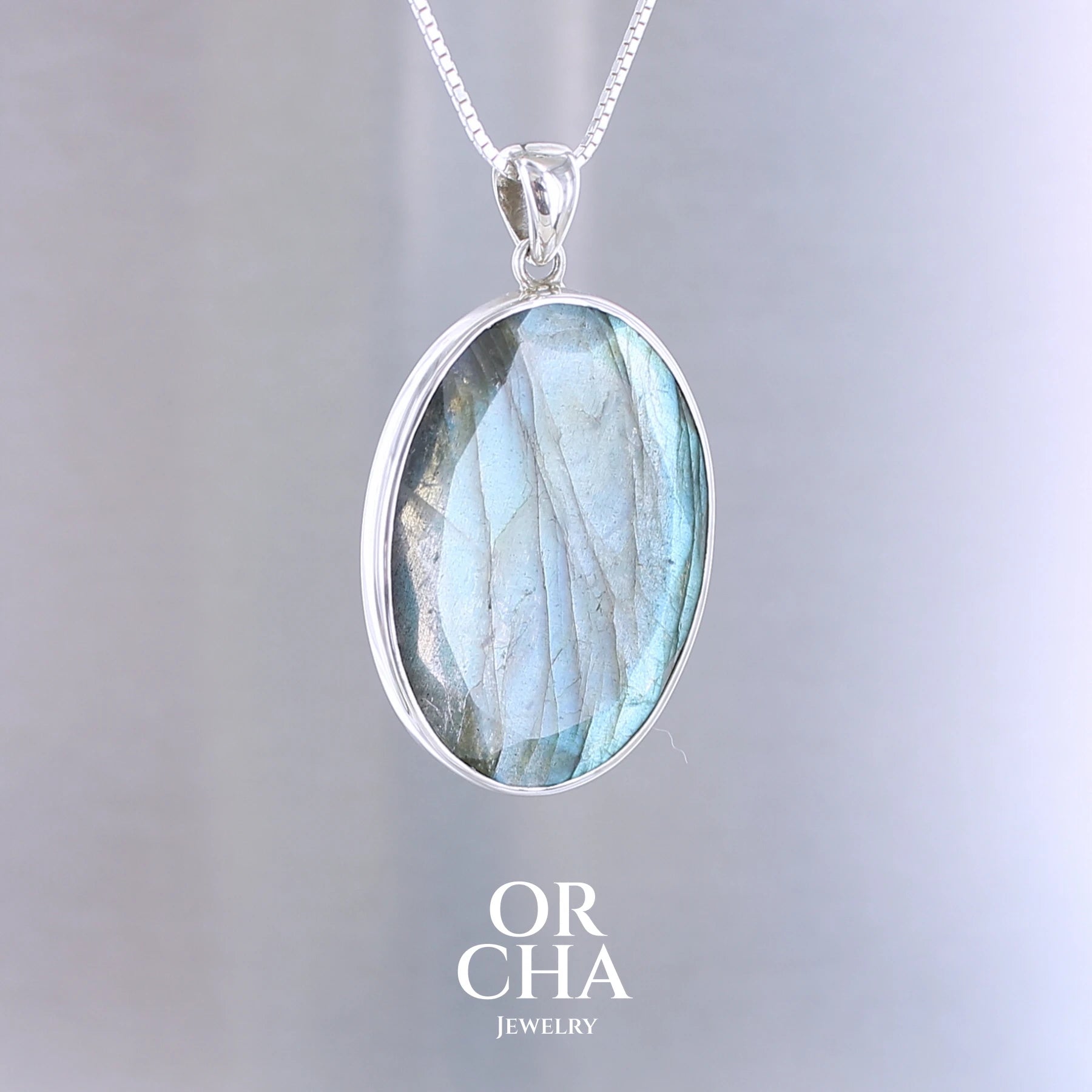 Pendentif ovale pour femme en argent massif serti d'une labradorite aux reflets bleus clairs, bleu vert selon la lumière. Pierre facettée naturelle translucide présentant des inclusions fréquents sur ce type de pierre. Bijoux unique, éthique et durable présenté dans un coffret de notre marque, prêt à offrir. Livraison offerte, certificat d'authenticité, service client.