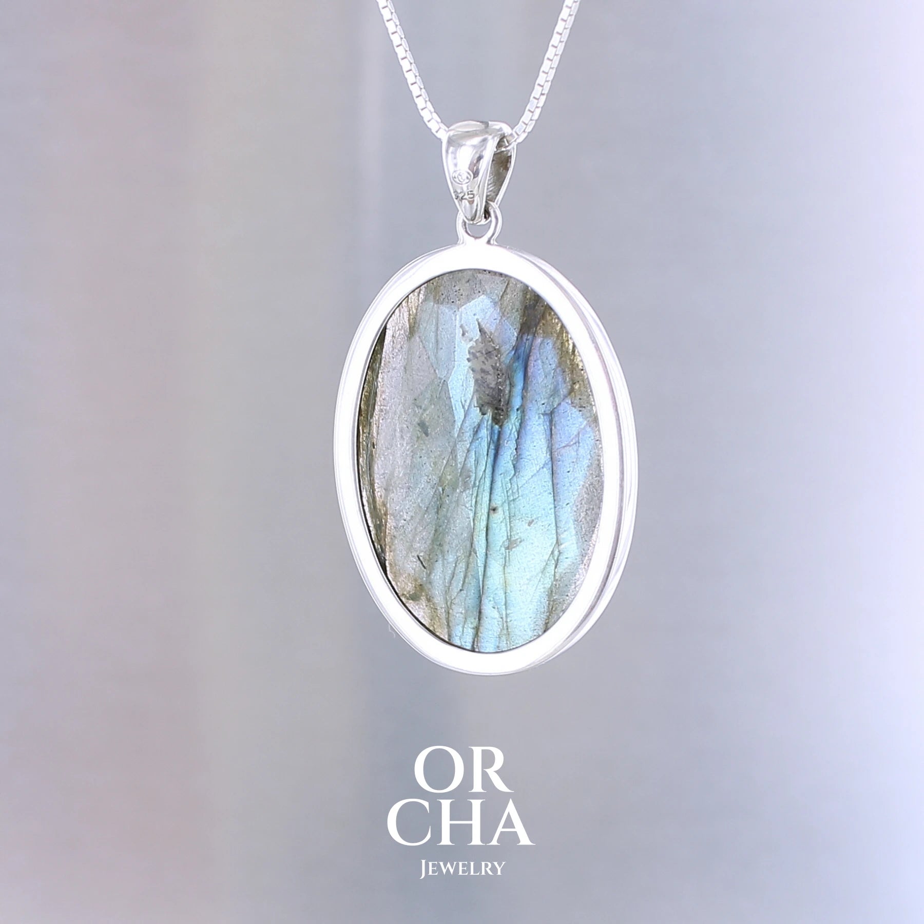 Pendentif ovale pour femme en argent massif serti d'une labradorite aux reflets bleus clairs, bleu vert selon la lumière. Pierre facettée naturelle translucide présentant des inclusions fréquents sur ce type de pierre. Bijoux unique, éthique et durable présenté dans un coffret de notre marque, prêt à offrir. Livraison offerte, certificat d'authenticité, service client.