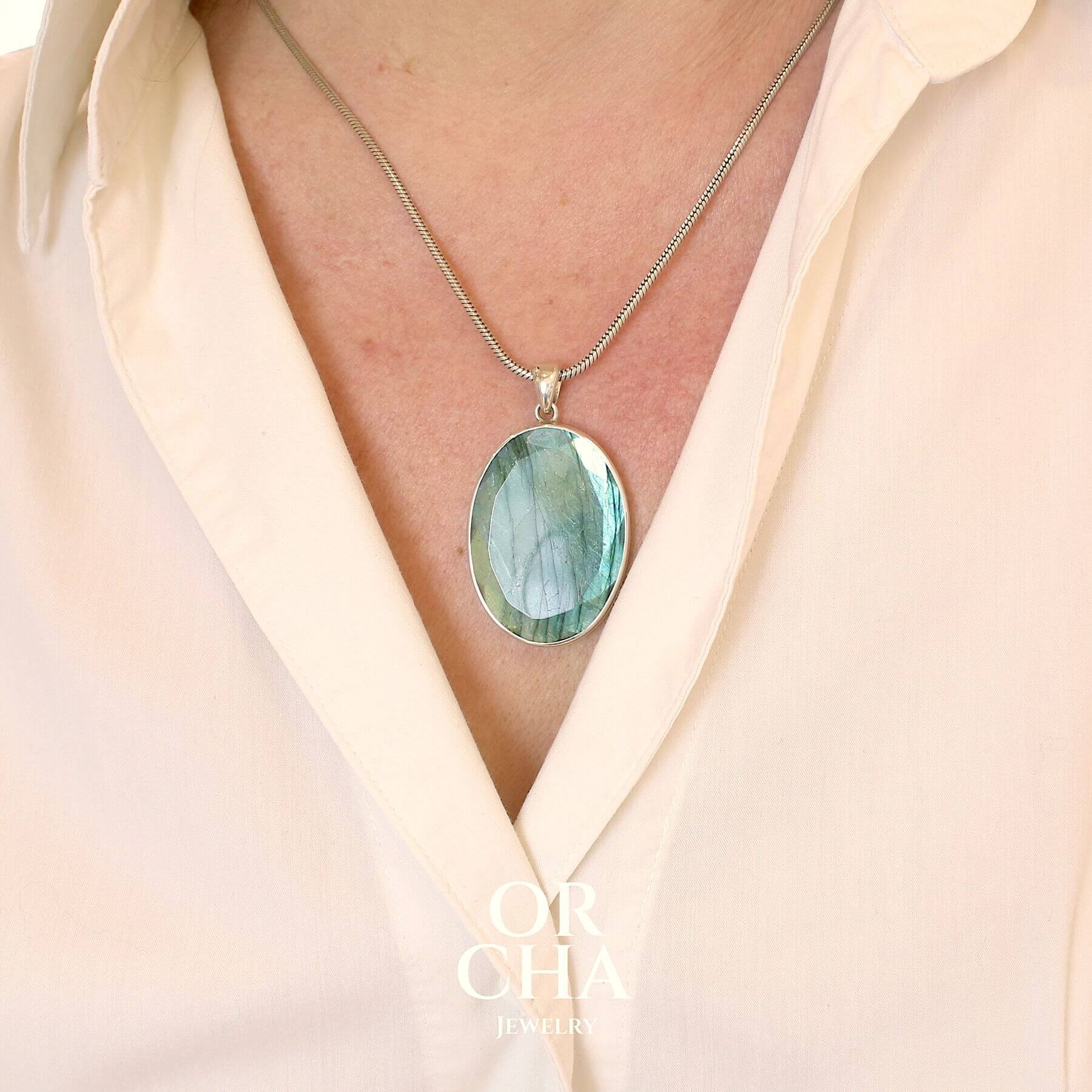 Pendentif ovale pour femme en argent massif serti d'une labradorite aux reflets bleus clairs, bleu vert selon la lumière. Pierre facettée naturelle translucide présentant des inclusions fréquents sur ce type de pierre. Bijoux unique, éthique et durable présenté dans un coffret de notre marque, prêt à offrir. Livraison offerte, certificat d'authenticité, service client.