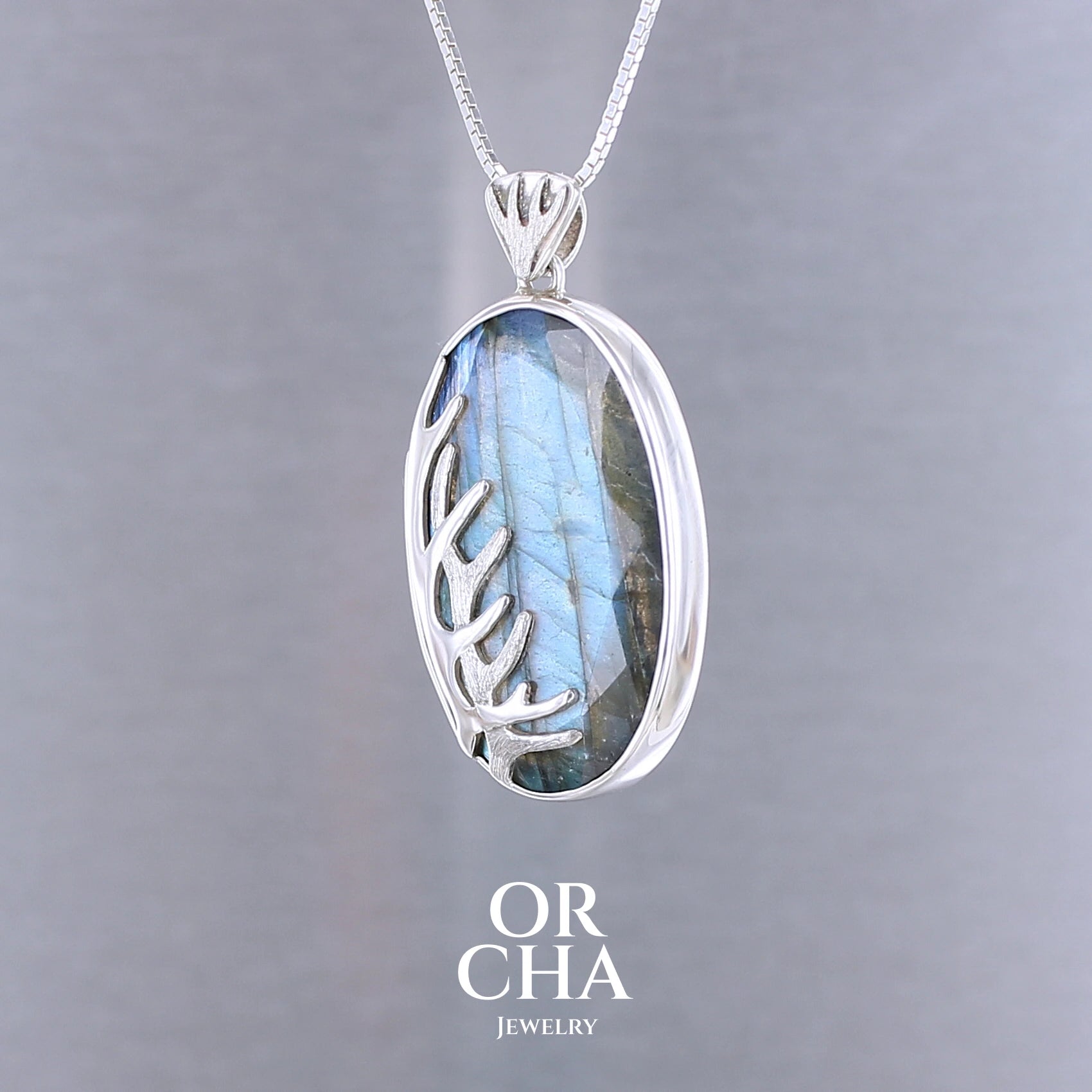 Pendentif pour femme en argent massif sertie d'une labradorite aux reflets bleus, Une ramure de cerf sculptée en argent penchasse la pierre. Pierre facettée naturelle translucide présentant des inclusions fréquents sur ce type de pierre. Bijoux unique, éthique et durable présenté dans un coffret de notre marque, prêt à offrir. Livraison offerte, certificat d'authenticité, service client.