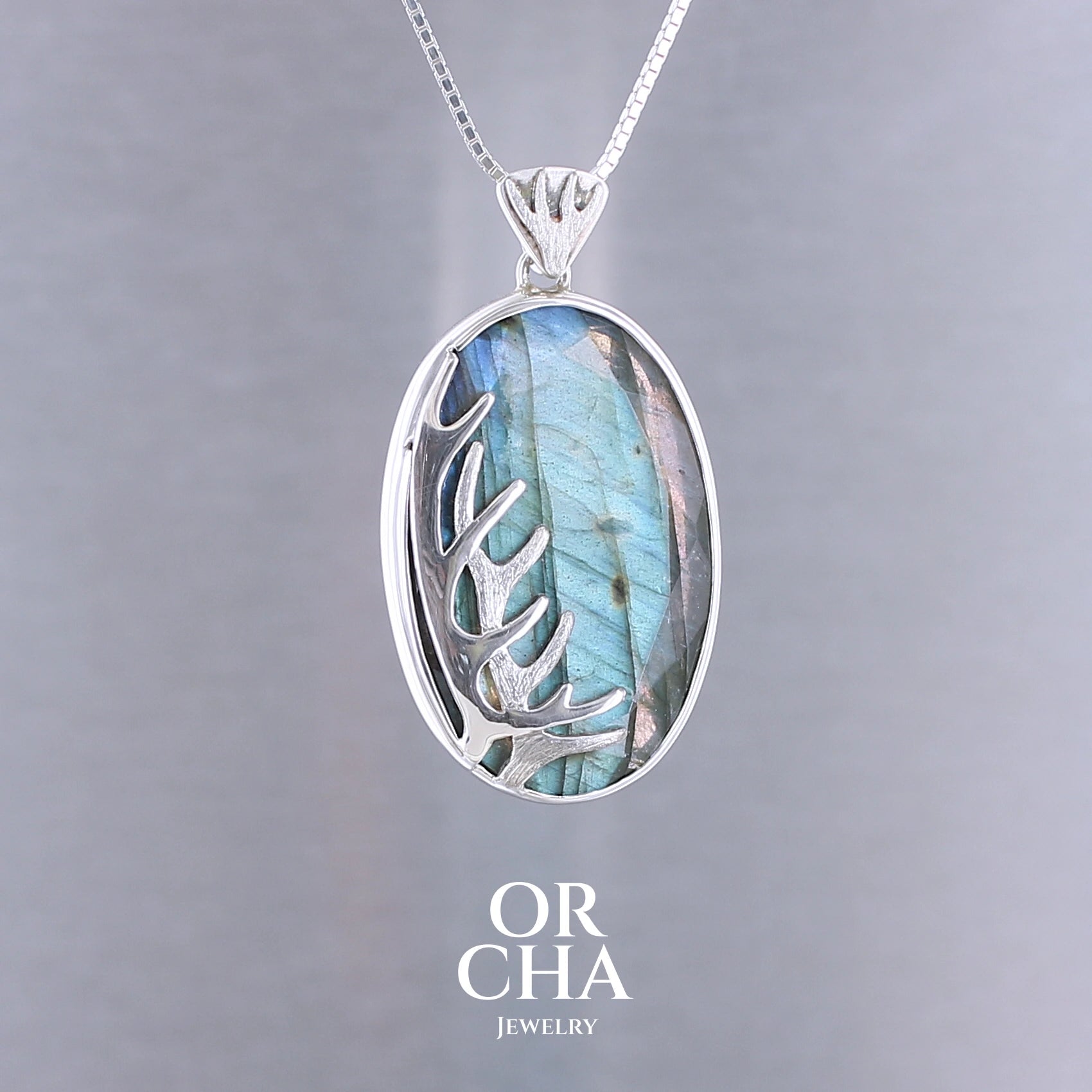 Pendentif pour femme en argent massif sertie d'une labradorite aux reflets bleus, Une ramure de cerf sculptée en argent penchasse la pierre. Pierre facettée naturelle translucide présentant des inclusions fréquents sur ce type de pierre. Bijoux unique, éthique et durable présenté dans un coffret de notre marque, prêt à offrir. Livraison offerte, certificat d'authenticité, service client.