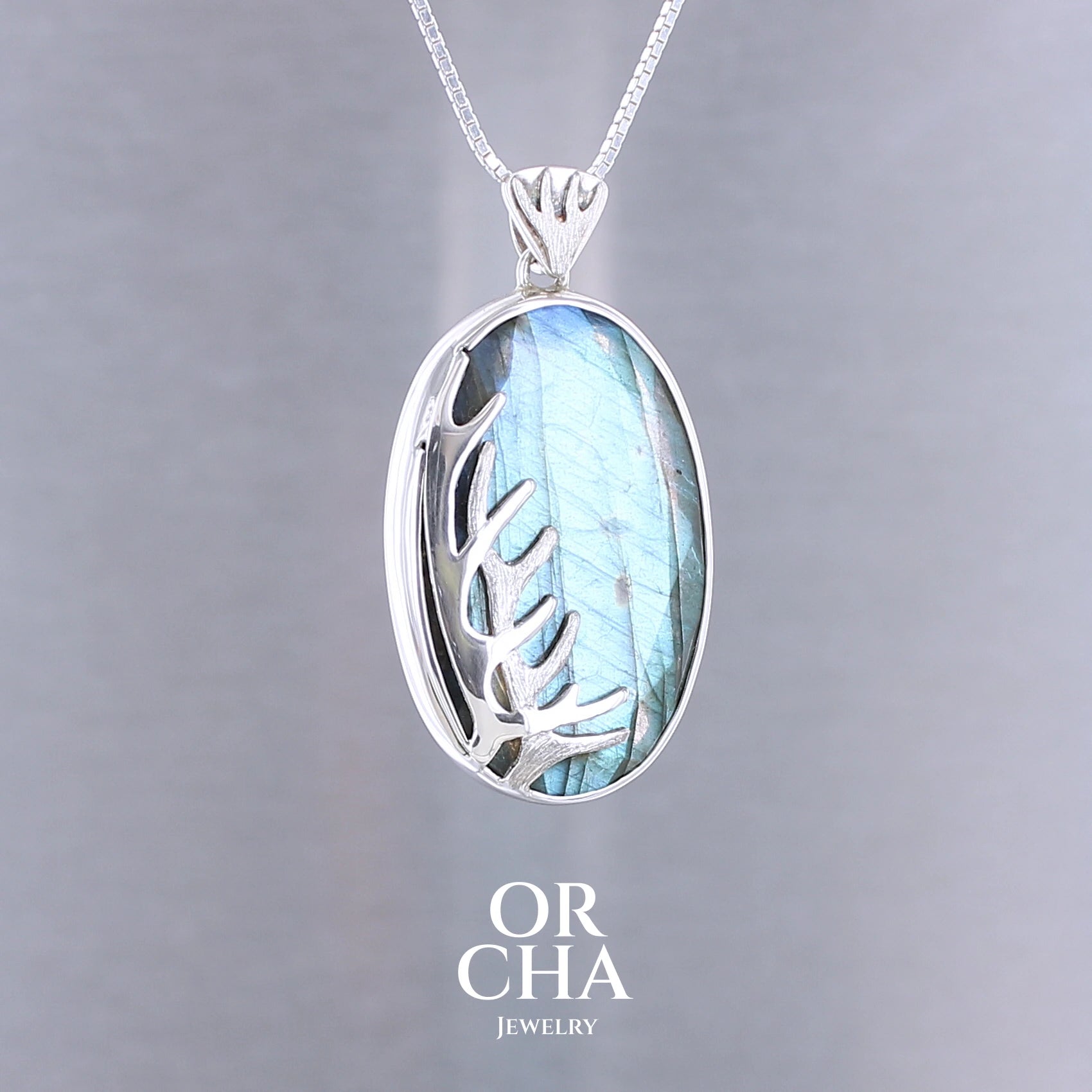 Pendentif pour femme en argent massif sertie d'une labradorite aux reflets bleus, Une ramure de cerf sculptée en argent penchasse la pierre. Pierre facettée naturelle translucide présentant des inclusions fréquents sur ce type de pierre. Bijoux unique, éthique et durable présenté dans un coffret de notre marque, prêt à offrir. Livraison offerte, certificat d'authenticité, service client.