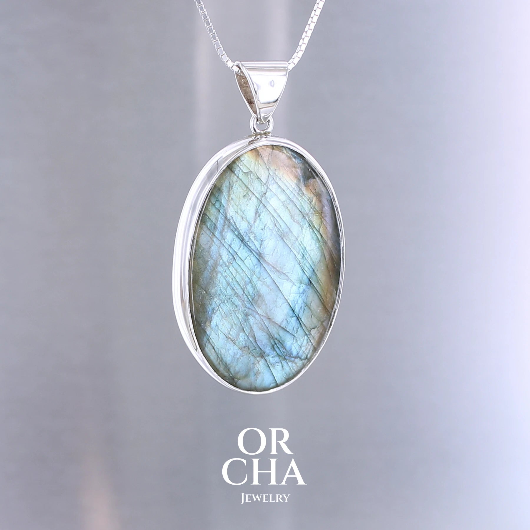 Pendentif pour femme en argent massif sertie d'une labradorite aux reflets bleu turquoise selon la lumière. Pierre cabochon naturelle translucide présentant des inclusions fréquents sur ce type de pierre. Bijoux unique, éthique et durable présenté dans un coffret de notre marque, prêt à offrir. Livraison offerte, certificat d'authenticité, service client.