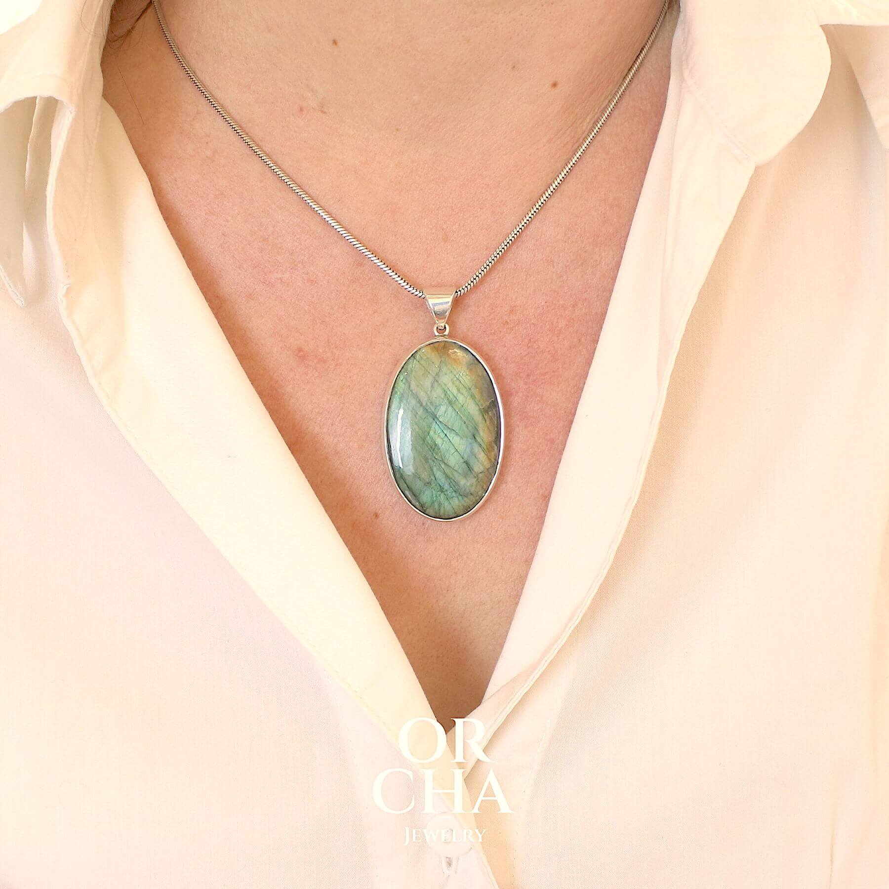 Pendentif pour femme en argent massif sertie d'une labradorite aux reflets bleu turquoise selon la lumière. Pierre cabochon naturelle translucide présentant des inclusions fréquents sur ce type de pierre. Bijoux unique, éthique et durable présenté dans un coffret de notre marque, prêt à offrir. Livraison offerte, certificat d'authenticité, service client.