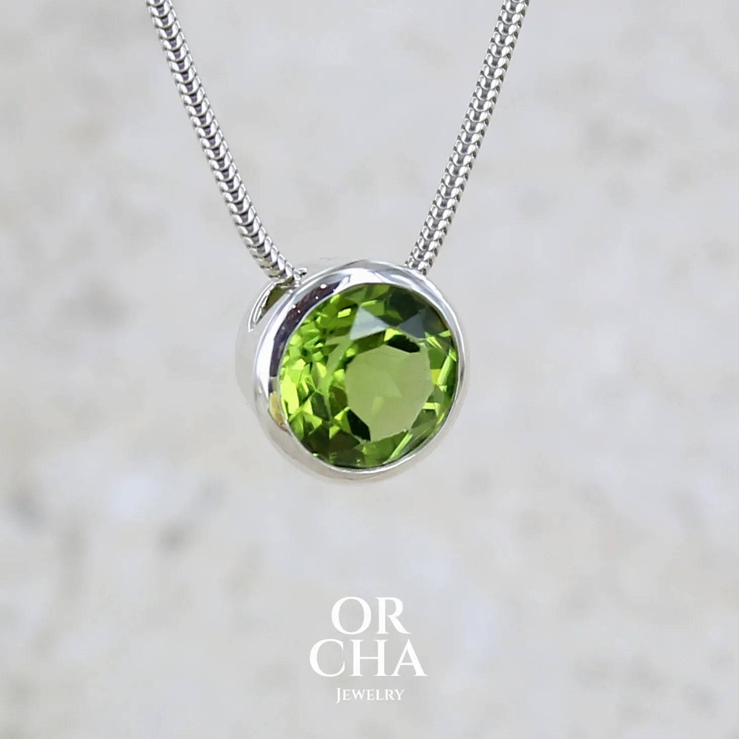 collier solitaire pour femme en argent massif serti d'un Péridot facettée de 4 carats. Pierre de forme ronde de qualité transparente, propre à l'oeil. Pierre naturelle de couleur vert olive doré intense et lumineuse. Pendentif monté sur une chaine en argent sterling de type maille serpent de 0,43 mm d'épaisseur et de 40 cm de longueur. Bijoux unique réalisé par Orchajewelry.