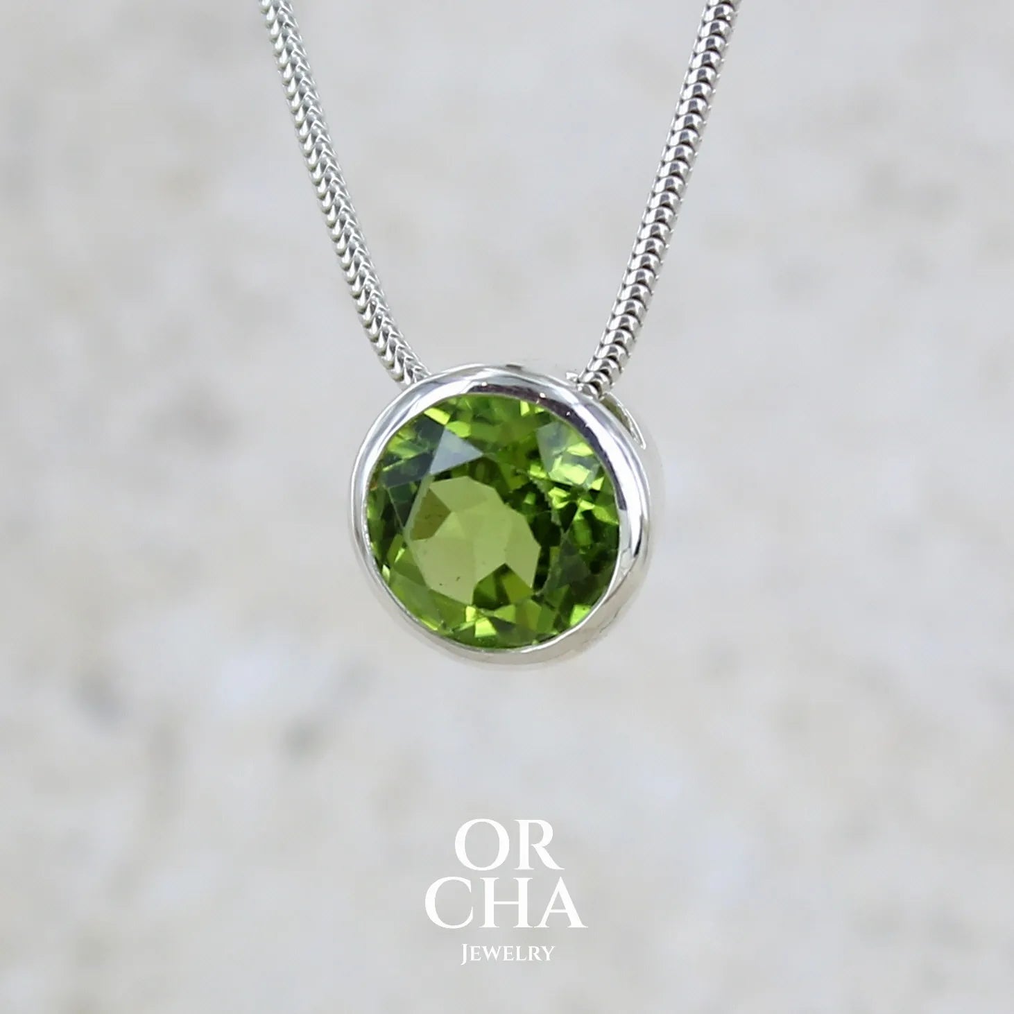 collier solitaire pour femme en argent massif serti d'un Péridot facettée de 4 carats. Pierre de forme ronde de qualité transparente, propre à l'oeil. Pierre naturelle de couleur vert olive doré intense et lumineuse. Pendentif monté sur une chaine en argent sterling de type maille serpent de 0,43 mm d'épaisseur et de 40 cm de longueur. Bijoux unique réalisé par Orchajewelry.