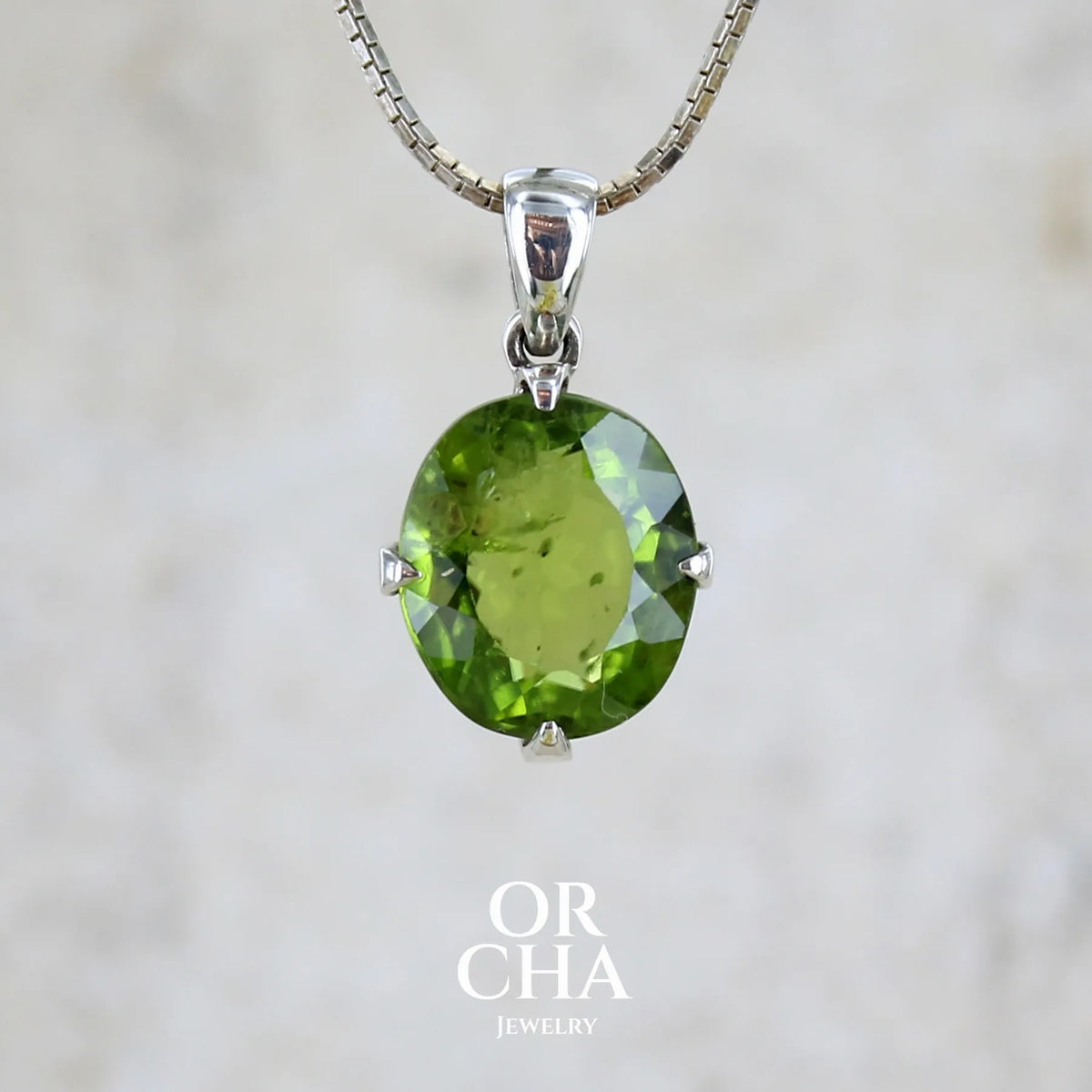 Pendentif pour femme en argent massif serti d'un péridot de couleur vert olive doré intense. Pierre taillée, de forme ovale, transparente présentant de nombreuse inclusions. Bijou unique réalisé par Orchajewelry