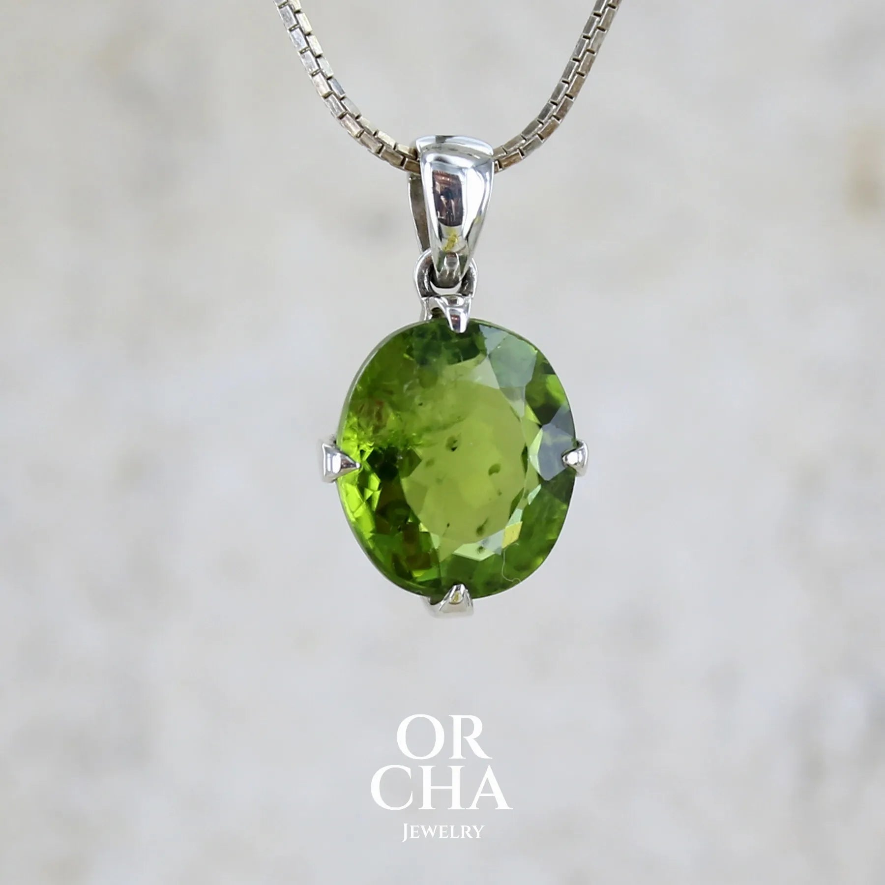 Pendentif pour femme en argent massif serti d'un péridot de couleur vert olive doré intense. Pierre taillée, de forme ovale, transparente présentant de nombreuse inclusions. Bijou unique réalisé par Orchajewelry