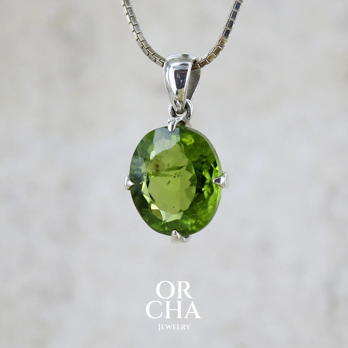 Pendentif pour femme en argent massif serti d'un péridot de couleur vert olive doré intense. Pierre taillée, de forme ovale, transparente présentant de nombreuse inclusions. Bijou unique réalisé par Orchajewelry