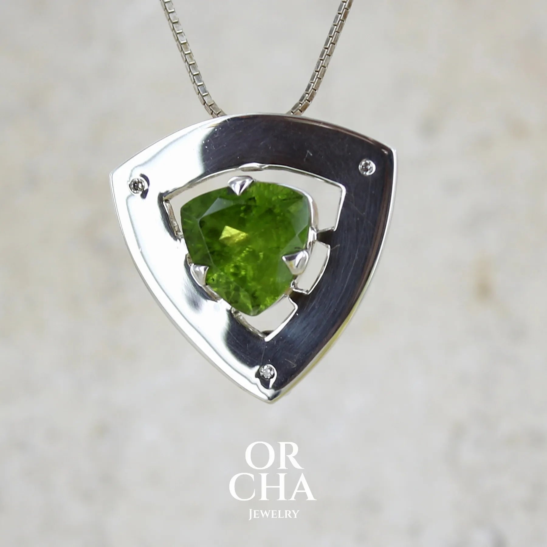 Pendentif contemporain pour femme en argent massif serti d'un péridot de couleur vert olive doré intense et de petits diamants. Pierre taillée, de forme triangulaire, transparente présentant de nombreuse inclusions. Bijou unique réalisé par Orchajewelry
