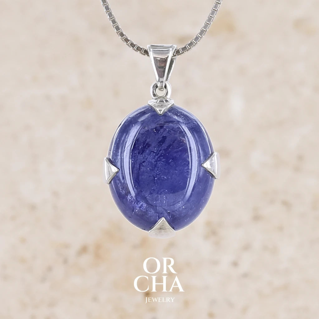 pendentif pour femme en argent massif serti griffe avec cabochon de Tanzanite de couleur bleu lavande foncé profond et intense . Pierre transparente présentant des inclusions. Pierre ayant subit un traitement de chauffe, traitement admis et fréquent en gemmologie pour ce type de pierre . Bijoux unique, éthique et durable présenté dans un coffret de notre marque, prêt à offrir. Livraison offerte, certificat d'authenticité, service client.