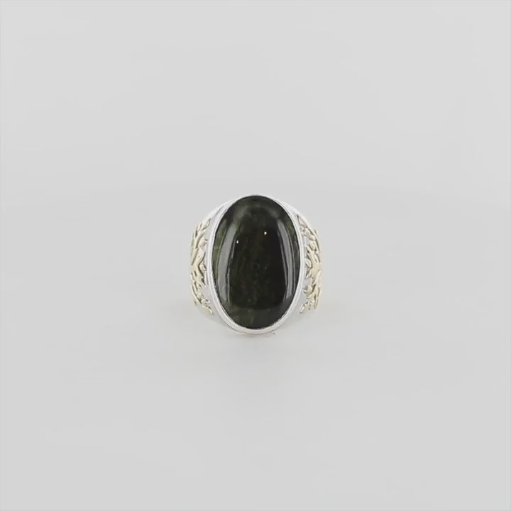 Bague pour homme en argent massif et or 18k où s'illustrent de chaque cotés de la bague des Arbres de vies en or. Cette bague est sertie d'un cabochon de moldavite de couleur vert foncé. Pierre naturelle transparente qui laisse voir le fond de la pierre laissé brute. Taille 64. Bijoux unique, éthique et durable présenté dans un coffret de notre marque, prêt à offrir. Livraison offerte, certificat d'authenticité, service client.