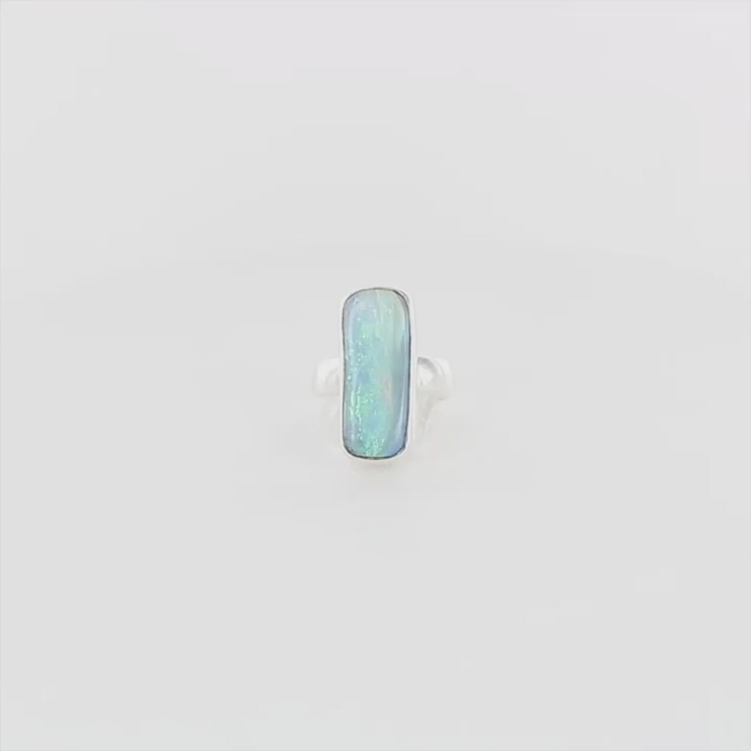 Bague en argent massif, avec une grande opale boulder rectangulaire sertie en cabochon. La pierre présente des reflets irisés bleu-vert intenses, ponctués de touches orangées. Le métal est lisse et poli, avec un anneau droit, épais et solide. Bague réalisée en taille 60. Bijoux unique, éthique et durable présenté dans un coffret de notre marque, prêt à offrir. Livraison offerte, certificat d'authenticité, service client.