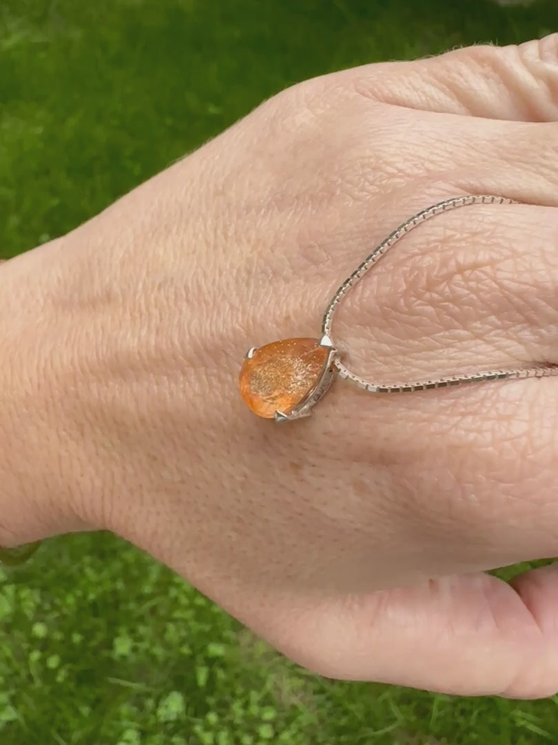 Collier solitaire pour femme en argent massif serti d'une pierre de soleil. Pierre de couleur orange facettée en forme de goutte, qualité transparente à  inclusions scintillantes dorées orangées. Pendentif monté sur une chaine en argent sterling de type maille carrée miroir de 0,94 mm d'épaisseur et de 40 cm de longueur. Bijoux unique, éthique et durable présenté dans un coffret de notre marque, prêt à offrir. Livraison offerte, certificat d'authenticité, service client.