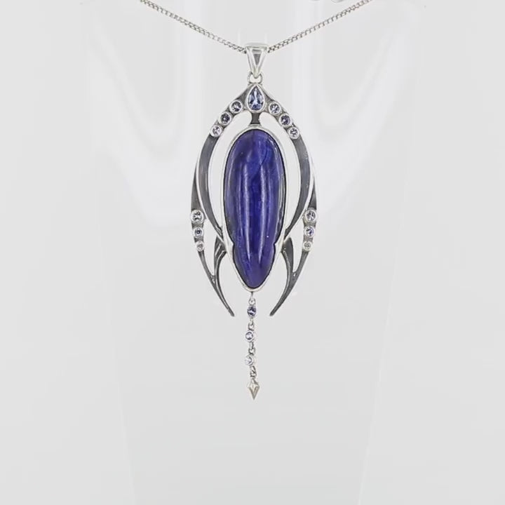 Pendentif contemporain en argent massif représentant une forme organique stylisée. Il est orné d’une azurite bleu profond de forme ovale allongée, encadrée de deux structures symétriques serties de petites tanzanite rondes violettes. Une ligne de pierres descend sous la pierre centrale, se terminant par un élément pointu sculpté. Bijoux unique, éthique et durable présenté dans un coffret de notre marque, prêt à offrir. Livraison offerte, certificat d'authenticité, service client.