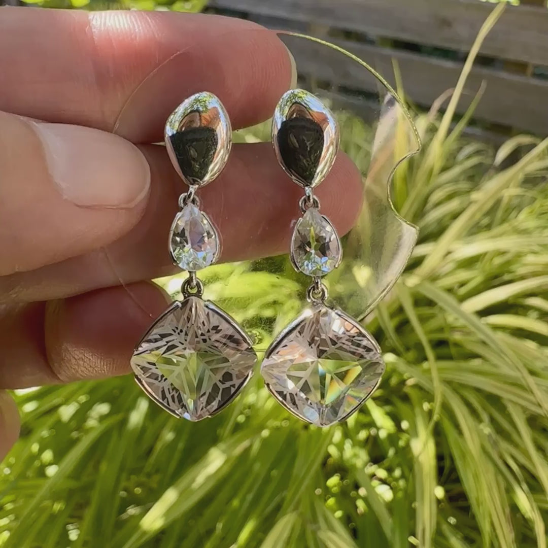 Boucles d'oreilles pendantes pour femme en argent massif serties de Cristals de roche gravés d'étoiles et de topazes blanches. Pierres facettée de forme carrée et goutte de qualité transparente, propre à l'oeil. Pierre naturelle incolore et blanche sur les parties gravées. Boucles de 3,7 cm de long. Bijoux unique, éthique et durable présenté dans un coffret de notre marque, prêt à offrir. Livraison offerte, certificat d'authenticité, service client.