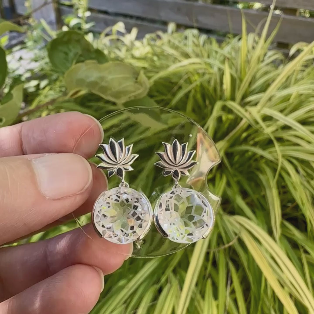 Boucles d'oreilles pour femme en argent massif sertie de Cristals de roche gravés de fleurs de vie. Pierres facettées de forme ronde de qualités transparentes, propre à l'oeil. Pierre naturelle incolore et blanche sur les parties gravées. Le clou des boucles représente un lotus. Bijoux unique, éthique et durable présenté dans un coffret de notre marque, prêt à offrir. Livraison offerte, certificat d'authenticité, service client.