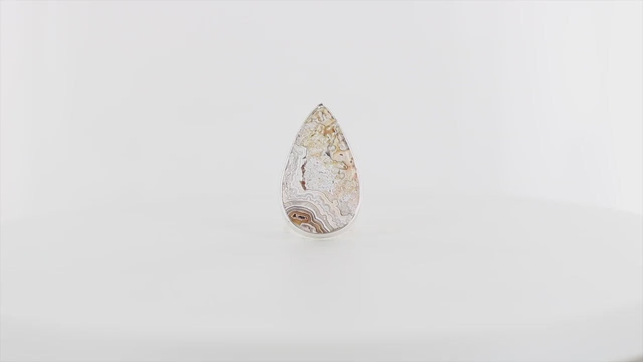Bague contemporaine en argent massif, sertie d’une grande pierre en forme de goutte polie : une agate crazy lace. La pierre présente des motifs naturels marbrés dans des tons beige, crème et ocre,marins. Bague réalisée en taille 55. Bijoux unique, éthique et durable présenté dans un coffret de notre marque, prêt à offrir. Livraison offerte, certificat d'authenticité, service client.