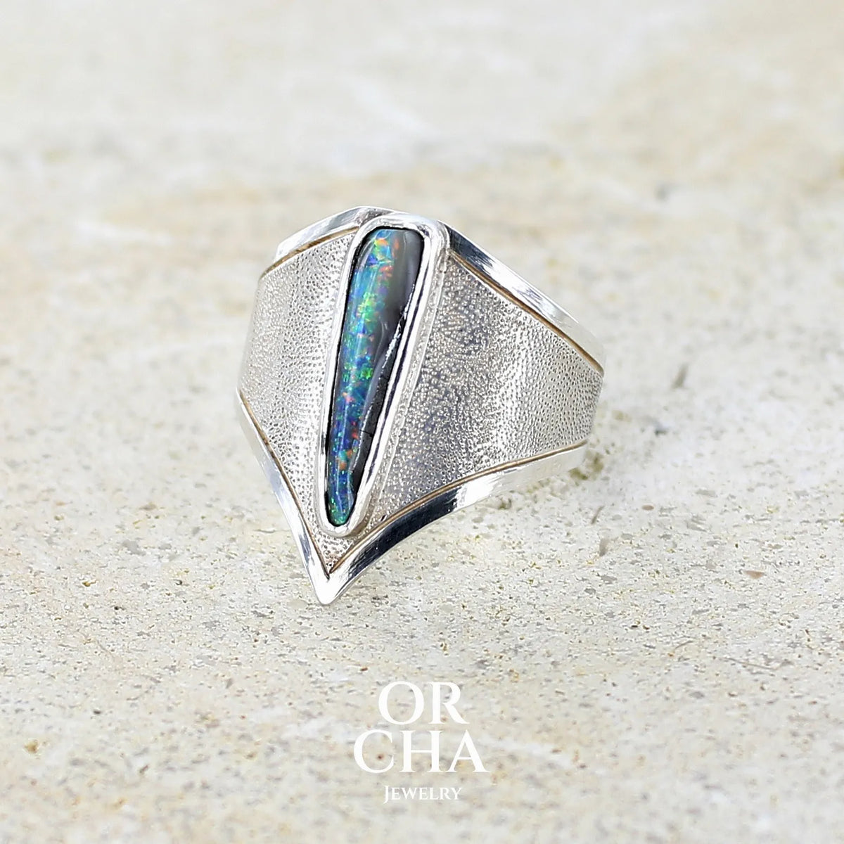 profil gauche d'une bague pour femme en argent massif 925 sertie d'une opale boulder aux feux multicolores bleus violet et verts. Cabochon d'opale massive naturelle taillée en forme d'aile. Pierre de qualité opaque. Bijoux unique réalisé en taille 57 par Orcha Jewelry