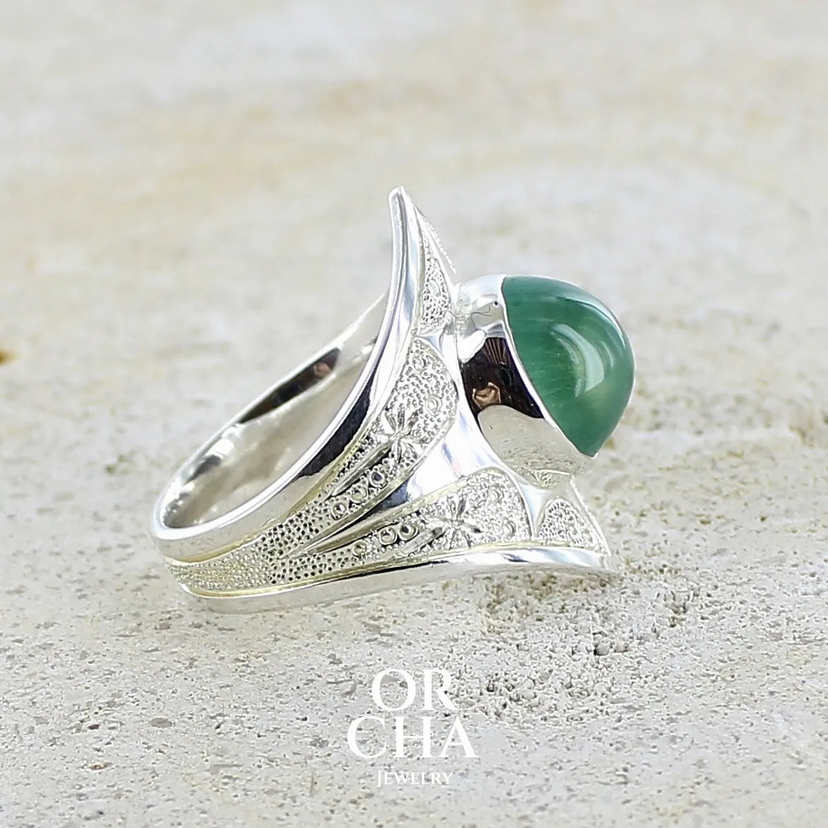 Profil d'une bague pour femme en argent massif sculptées d'étoiles et autres corps célestes sertie d'un cabochon ovale de préhnite de couleur verte pastel lumineuse. Pierre naturelle de qualité transparente présentant des inclusions. Bijoux unique réalisé en taille 57 par Orchajewelry.