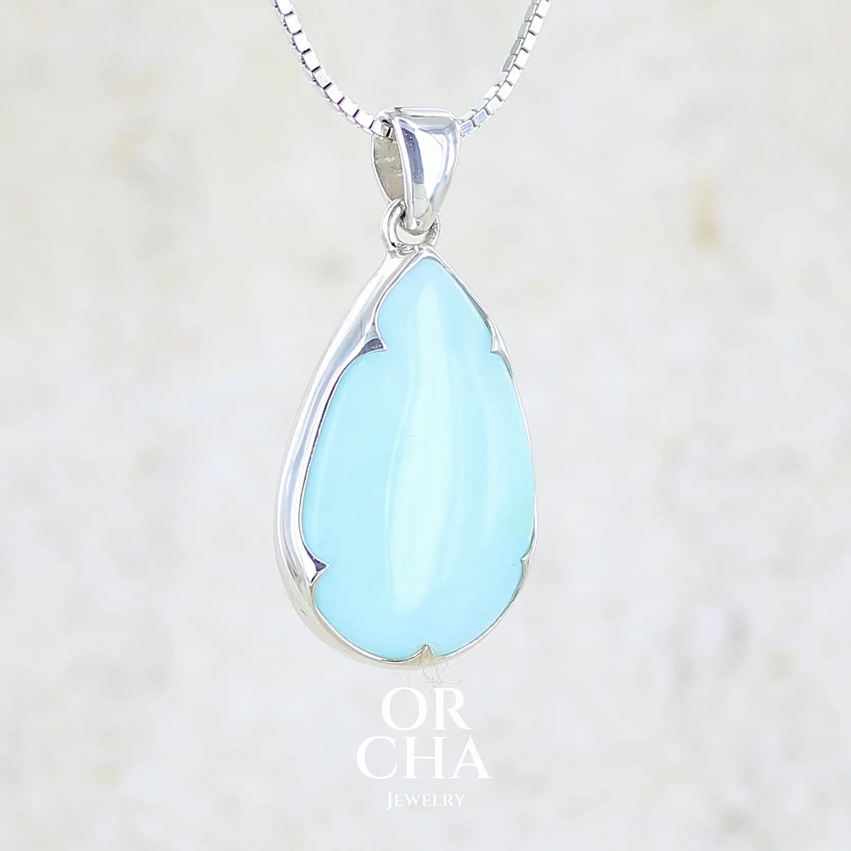 profil droit d'un pendentif en argent massif, sertie d'un cabochon d'opale bleue du Pérou de couleur bleu ciel clair. Pierre en forme de goutte. Pierre opaque et translucide. Bijoux unique, éthique et durable présenté dans un coffret de notre marque, prêt à offrir. Livraison offerte, certificat d'authenticité, service client.