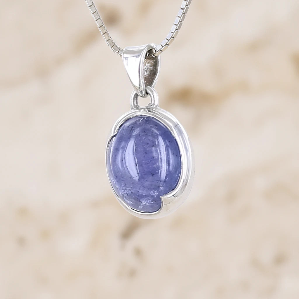 Profil gauche d'un pendentif pour femme en argent massif serti d'un cabochon de Tanzanite de couleur bleu lavande . Pierre translucide présentant des inclusions. Pierre ayant subit un traitement de chauffe, traitement admis et fréquent en gemmologie pour ce type de pierre . Bijoux unique, éthique et durable présenté dans un coffret de notre marque, prêt à offrir. Livraison offerte, certificat d'authenticité, service client.