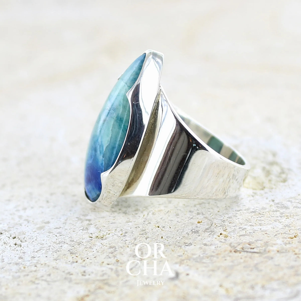 Profil d'une bague pour femme en argent massif sertie d'un cabochon d'afghane de couleur bleu et bleu gris vert. Pierre taillée en forme de goutte de qualité opaque à inclusions (petites fissures) en surface, fréquente et admise sur ce type de pierre. Bijou unique réalisée en taille 58 par Orchajewelry