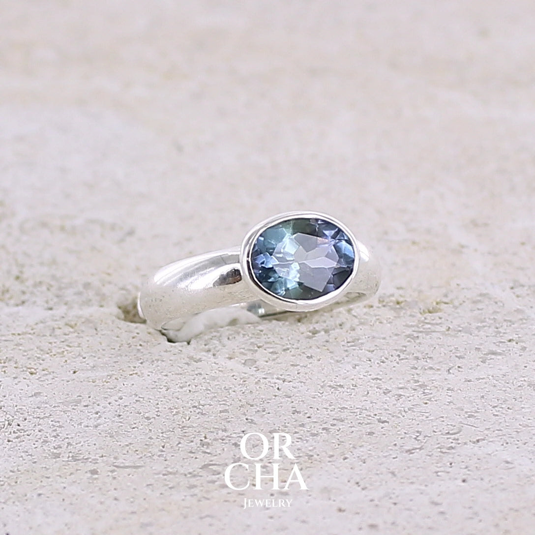 profil droit d'une bague solitaire pour femme en argent massif sertie d'une tanzanite bicolore. Pierre facettée de forme ovale de qualité transparente, propre à l'oeil. Pierre naturelle de couleur bleu verte et logés reflets violets. Bague réalisée en taille 50. Bijoux unique, éthique et durable présenté dans un coffret de notre marque, prêt à offrir. Livraison offerte, certificat d'authenticité, service client.