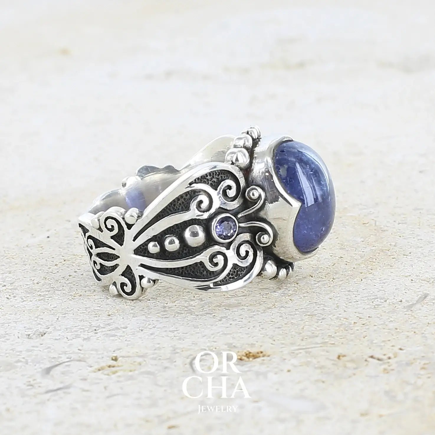 profil d'une bague en argent massif sculptées d'entrelacs de style celtique qui illustrent des papillons, sertie d'une Tanzanite. Pierre cabochon de forme ovale, de couleur bleu lavande foncé, de qualité transparente avec inclusions. Taille 56. Bijoux unique, éthique et durable présenté dans un coffret de notre marque, prêt à offrir. Livraison offerte, certificat d'authenticité, service client.