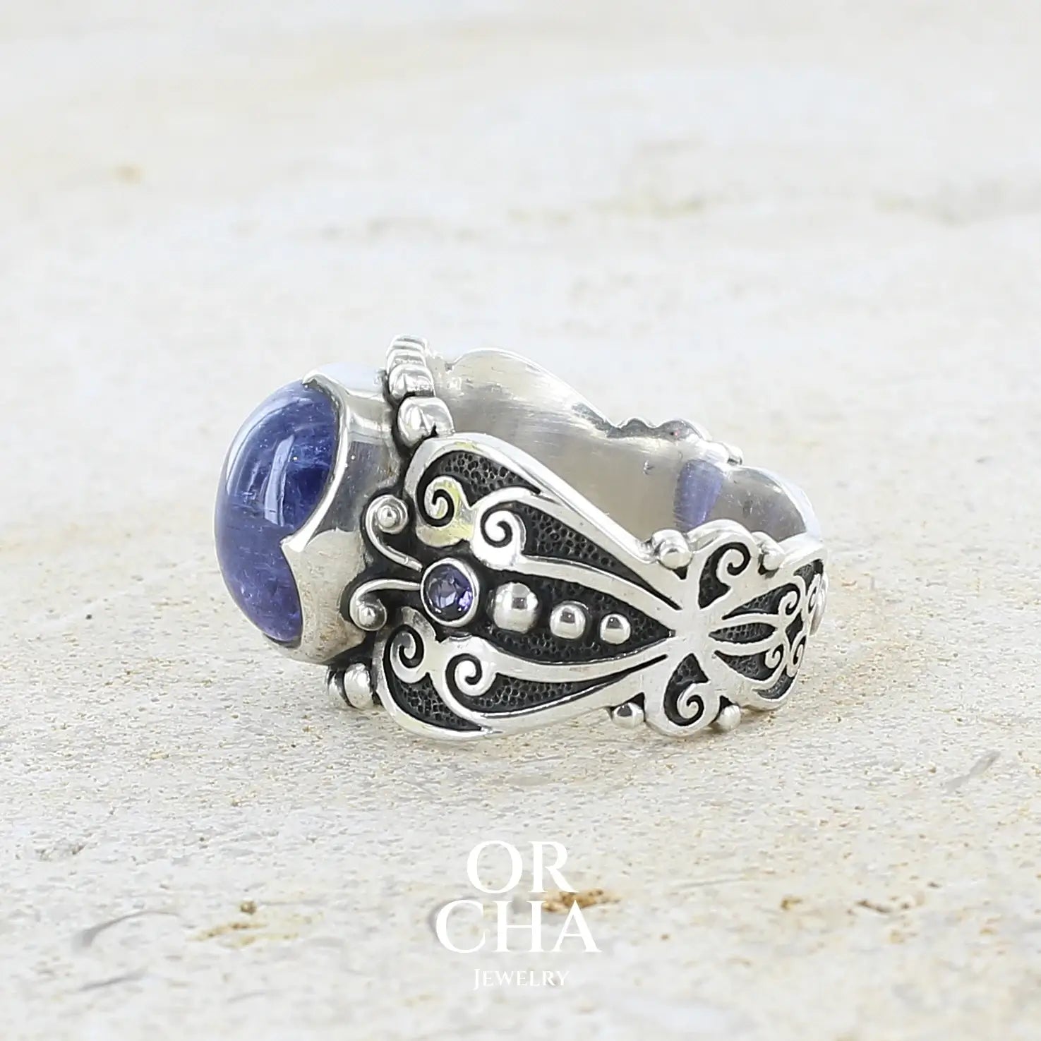 profil d'une bague en argent massif sculptées d'entrelacs de style celtique qui illustrent des papillons, sertie d'une Tanzanite. Pierre cabochon de forme ovale, de couleur bleu lavande foncé, de qualité transparente avec inclusions. Taille 56. Bijoux unique, éthique et durable présenté dans un coffret de notre marque, prêt à offrir. Livraison offerte, certificat d'authenticité, service client.