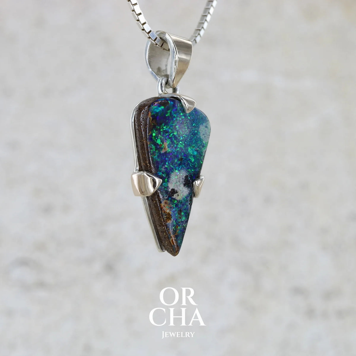 Profil droit d'un pendentif pour homme en or 9k et argent massif 925 serti d'une opale boulder aux feux multicolores bleus et verts. Tranche d'opale massive naturelle taillée en forme d'aile. Pierre de qualité opaque originaire d'Australie. Bijoux unique par Orcha Jewelry.