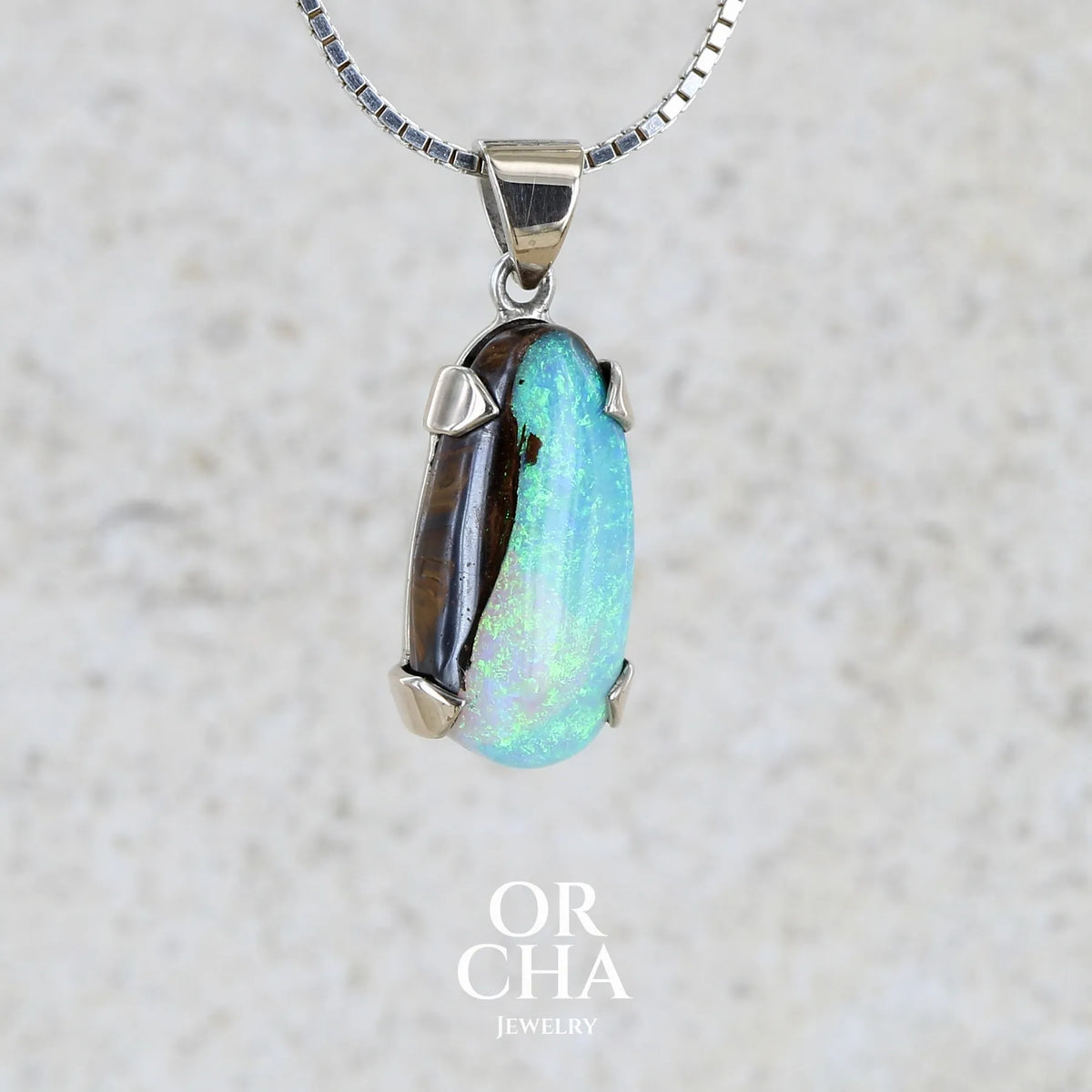 Profil droit d'un Pendentif pour femme en or 9k et argent massif serti d'une opale boulder cristal aux feux étoilés multicolores à dominantes bleu turquoise. Cabochon de 7 carat taillé en forme de goutte de qualité translucide. Opale massive australienne. Bijou unique réalisé par Orchajewelry