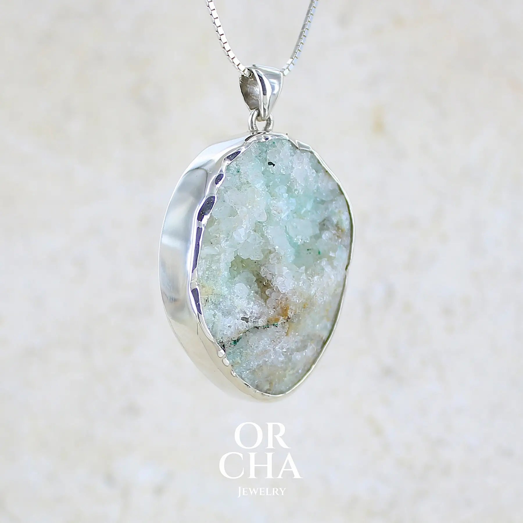 Profil droit d'un pendentif en argent massif serti d'un magnifique gemsilica druze: chrysocolle silicifiée recouverte de fins cristaux de quartz scintillant. Pierre de qualité opaque brute de forme ovale. Pierre naturelle originaire du Mexique de couleur verte bleutée claire.