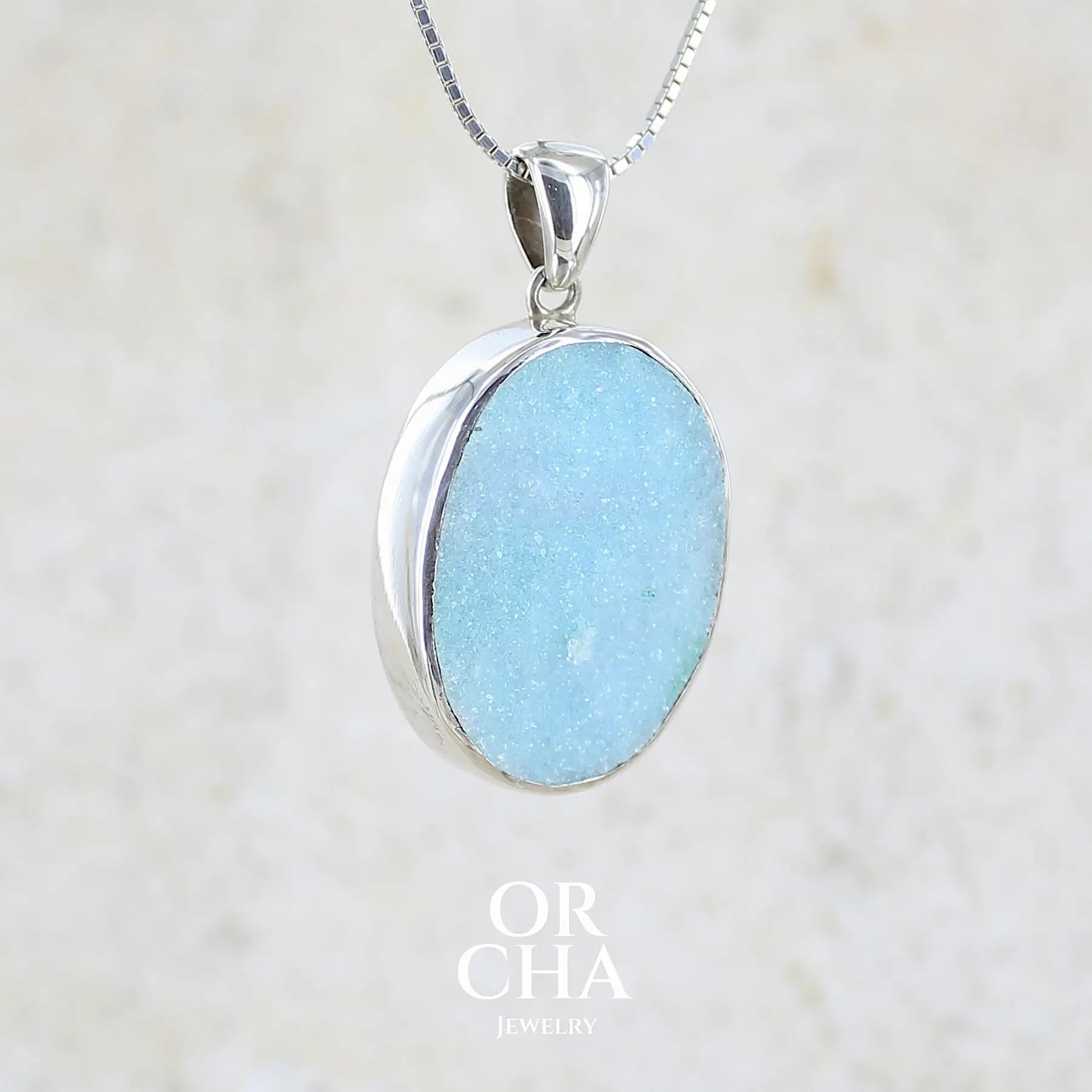 profil droit d'un pendentif pour femme en argent massif sertie d'un magnifique gemsilica druzy, chrysocolle silicifiée recouverte de fins cristaux de quartz scintillant. Pierre de qualité opaque taillée en tranche de forme ovale. Pierre naturelle originaire de République dominicaine du Congo de couleur bleu clair turquoise. pierre rare et unique