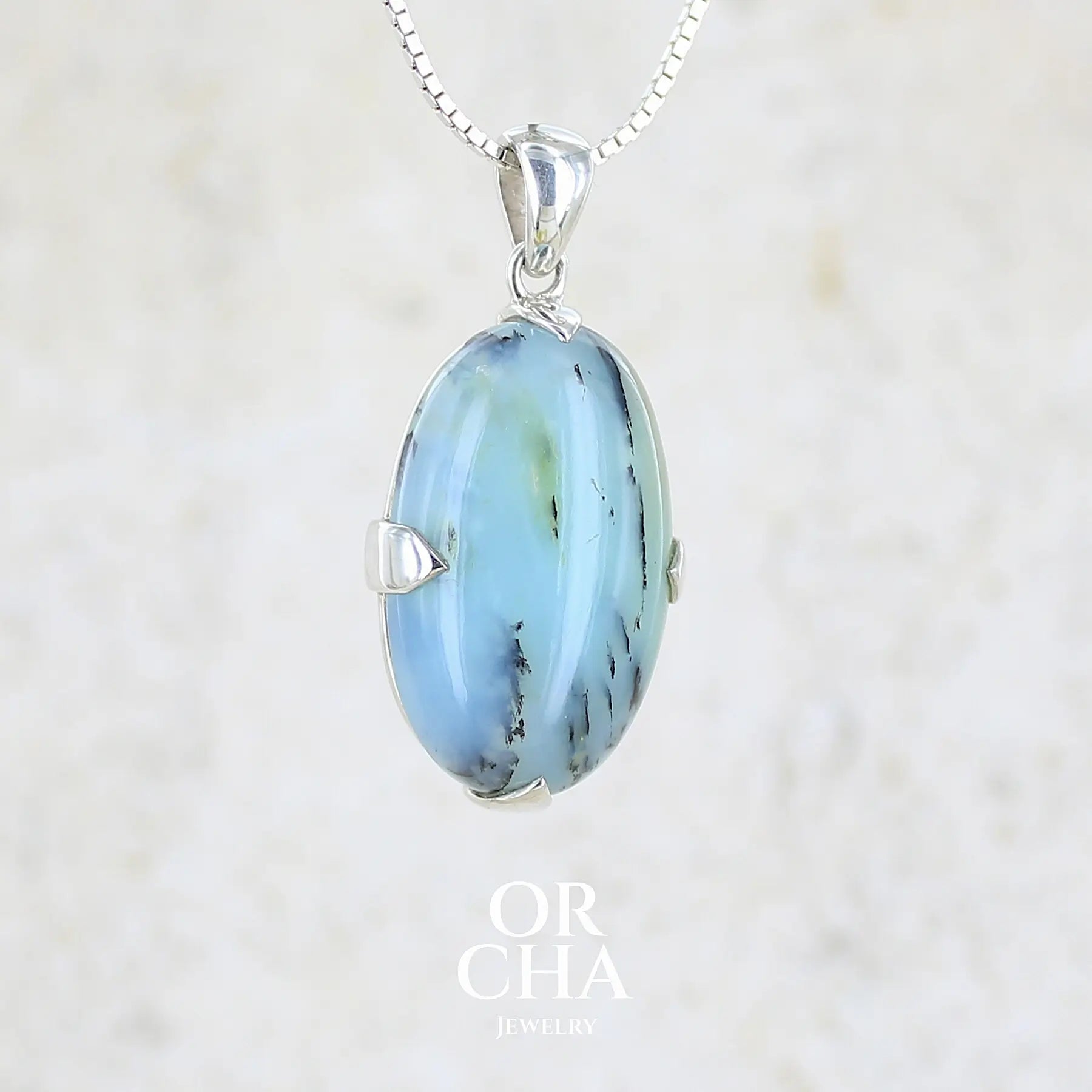 profil droit d'un pendentif en argent massif, sertie d'un cabochon ovale d'opale bleue du Pérou de couleur bleu laiteux à inclusions de dendrites noires. Pierre opaque et translucide. Bijoux unique, éthique et durable présenté dans un coffret de notre marque, prêt à offrir. Livraison offerte, certificat d'authenticité, service client.