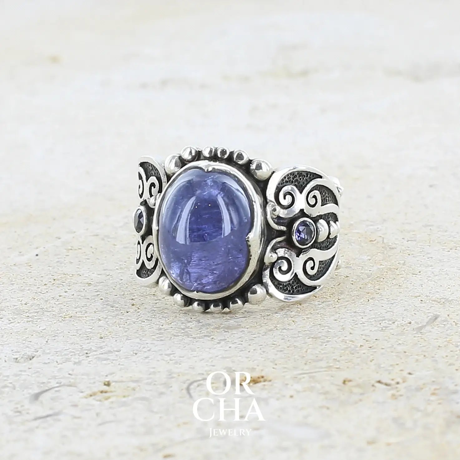 profile gauche d'une bague en argent massif sculptées d'entrelacs de style celtique qui illustrent des papillons, sertie d'une Tanzanite. Pierre cabochon de forme ovale, de couleur bleu lavande foncé, de qualité transparente avec inclusions. Taille 56. Bijoux unique, éthique et durable présenté dans un coffret de notre marque, prêt à offrir. Livraison offerte, certificat d'authenticité, service client.