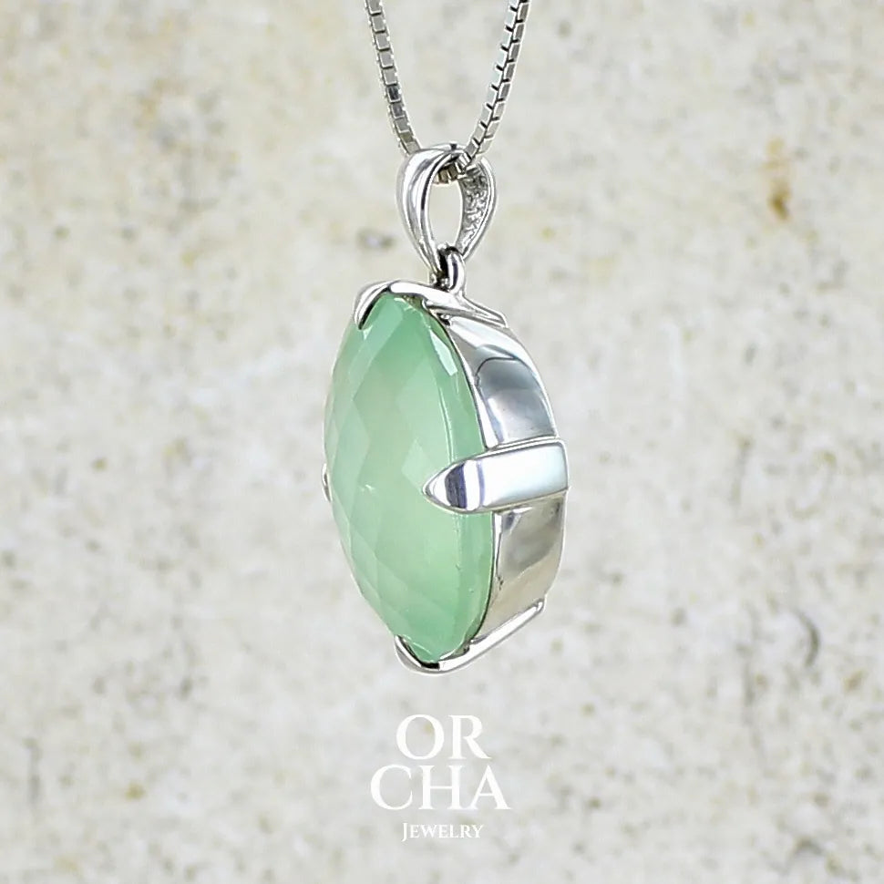 Profil gauche d'un pendentif ovale en argent massif, serti d'un cabochon facetté de préhnite de couleur verte jaune pastel. Pierre de qualité translucide comportant des inclusions. Bijoux unique par Orcha Jewelry