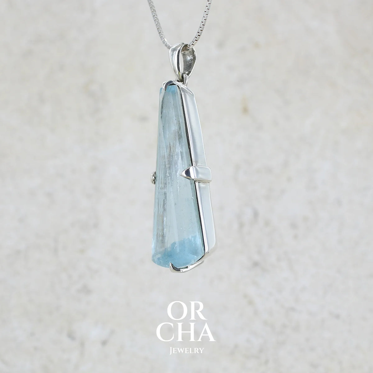 Profil gauche d'un pendentif en argent massif sertie d'une aigue marine taillée de 32 carats de couleur bleu clair profond et lumineux, pierre transparente avec inclusions. Pierre naturelle facettée de forme triangulaire allongé. Bijoux unique réalisée par Orchajewelry