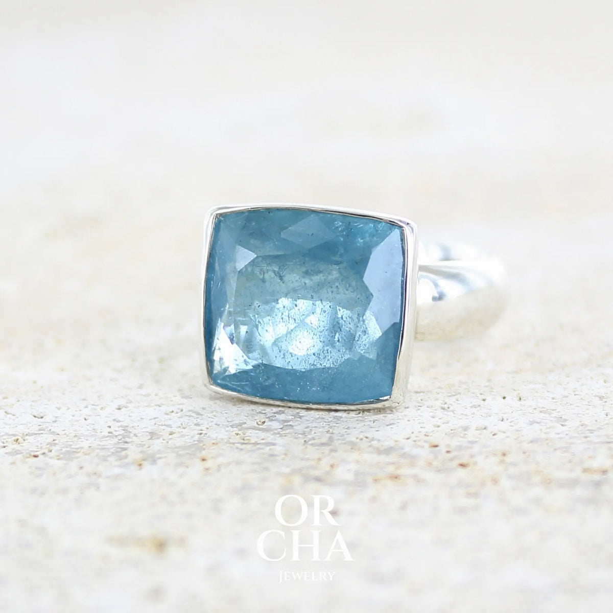 profile gauche d'une bague cocktail pour femme en argent massif sertie d'une aigue marine taillée de 10 carats de couleur bleue gris foncé, pierre transparente avec inclusions. Pierre naturelle facettée de forme rectangulaire. Bijoux unique réalisée en taille 60,5 par Orchajewelry