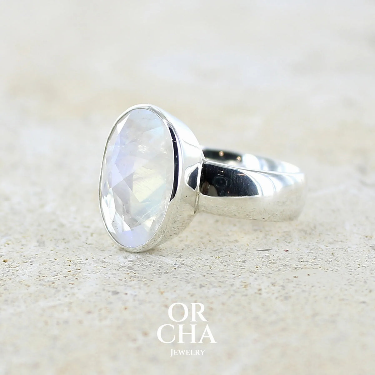 Profil gauche d'une Bague cocktail pour femme en argent massif 925 sertie d'une Labradorite blanche taillée de 6,7 carats incolore aux reflets bleutés et arc en ciel. Pierre transparente avec inclusions. Bijoux unique réalisée en taille 57 par Orchajewelry