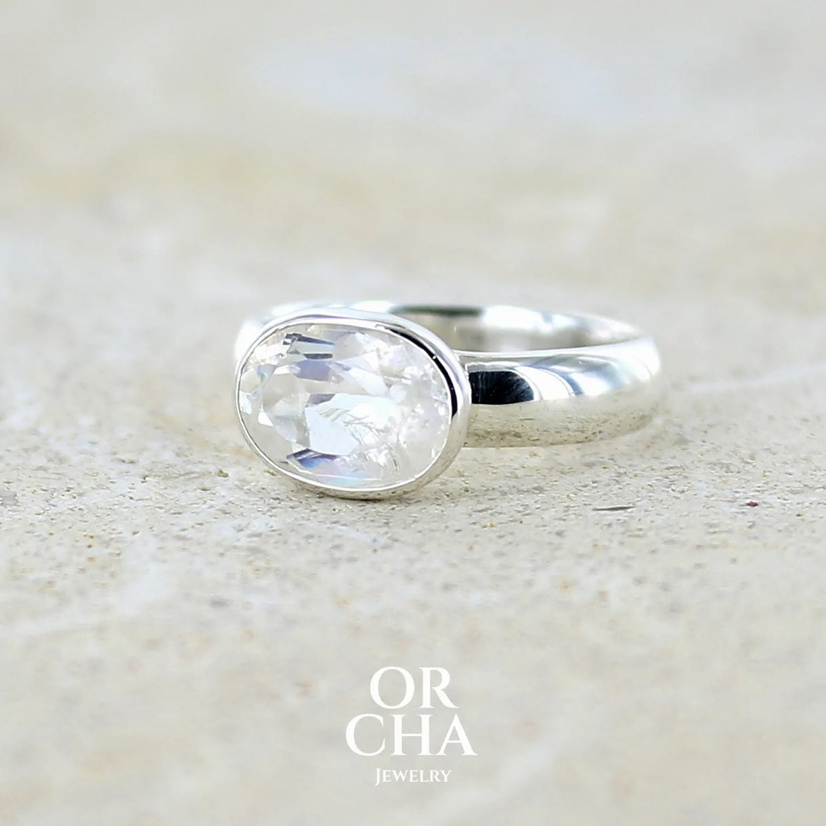 profil gauche d'une bague cocktail pour femme en argent massif 925 sertie d'une pierre de lune de Madagascar taillée de 2,18 carats, pierre incolore aux reflets orangés et arc en ciel. Pierre transparente avec inclusions. Bijoux unique réalisé en taille 52 par Orcha Jewelry